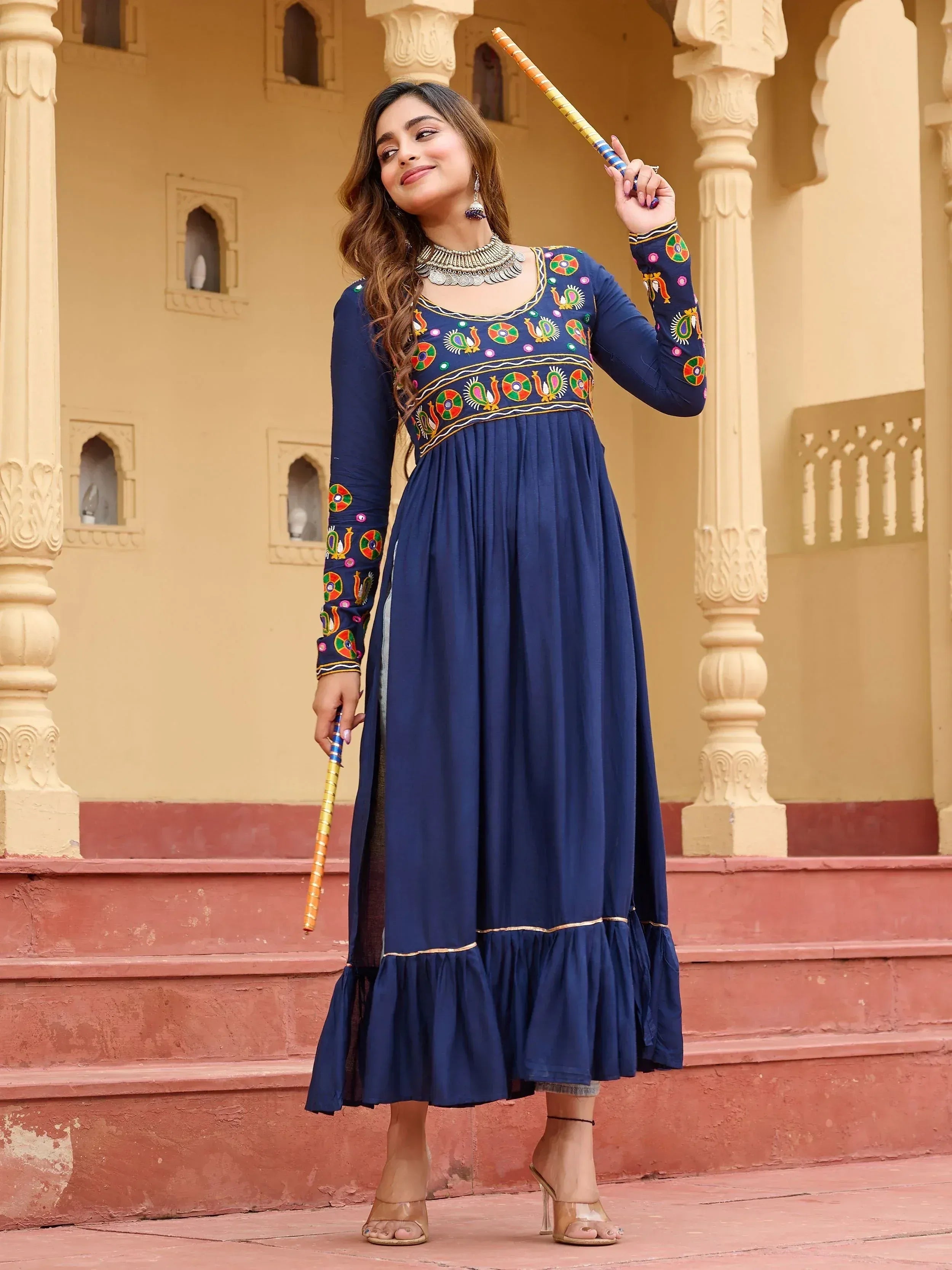 Navy blue embroidered ethnic gown with peacock motifs, paired with statement jewelry and heels.