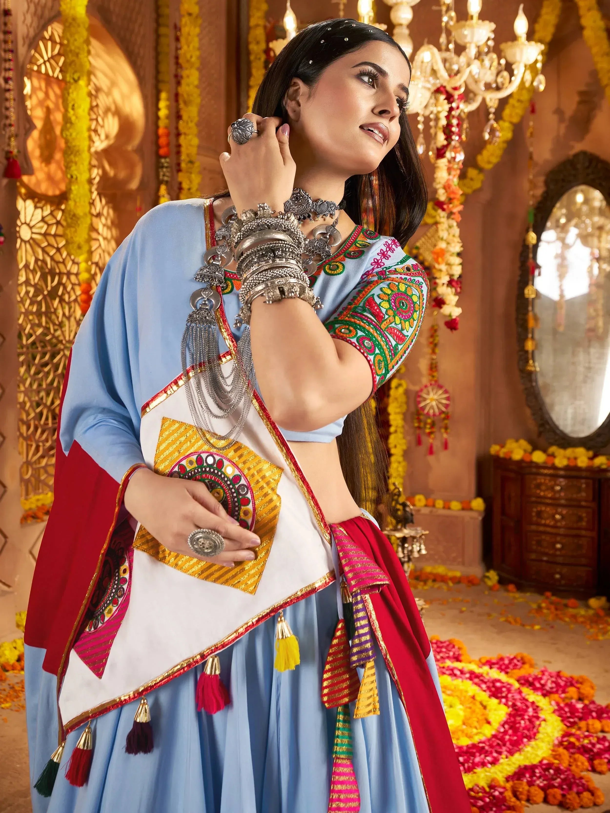 Woman in vibrant blue embroidered ethnic wear with silver jewelry, floral decor, and festive Indian attire