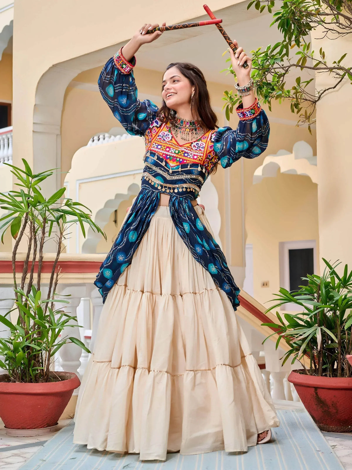 Woman in vibrant blue embroidered top and beige lehenga dancing with dandiya sticks, Indian ethnic wear