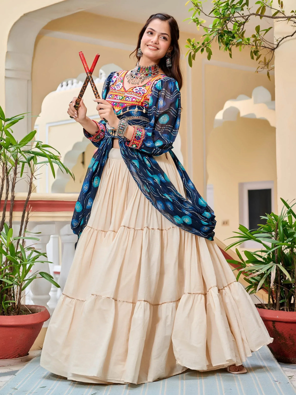 Woman in colorful embroidered Indian ethnic wear with dupatta, holding dandiya sticks, perfect for festive occasions.