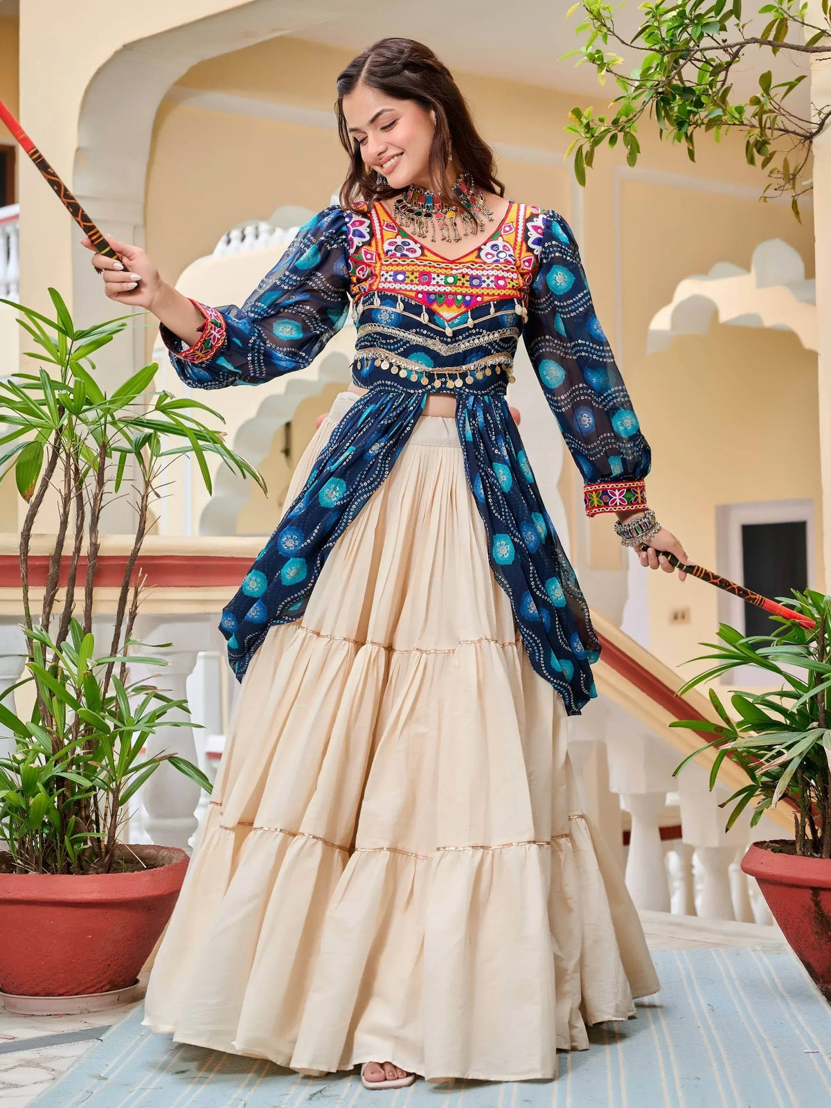Woman in colorful embroidered Indian ethnic wear with blue blouse and cream lehenga, holding sticks