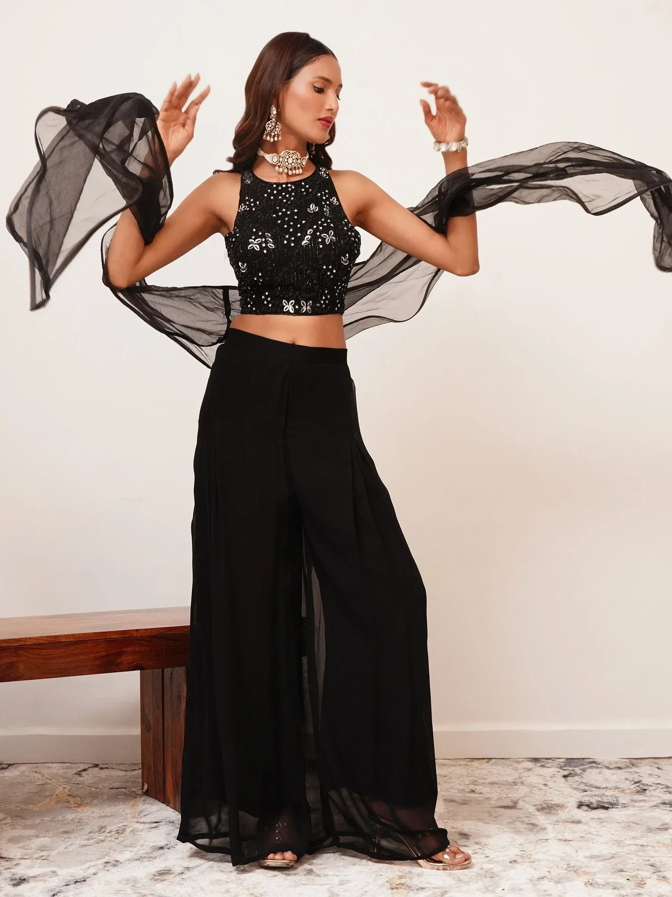 Woman in black sequined ethnic crop top, wide-leg pants, sheer dupatta, and statement jewelry