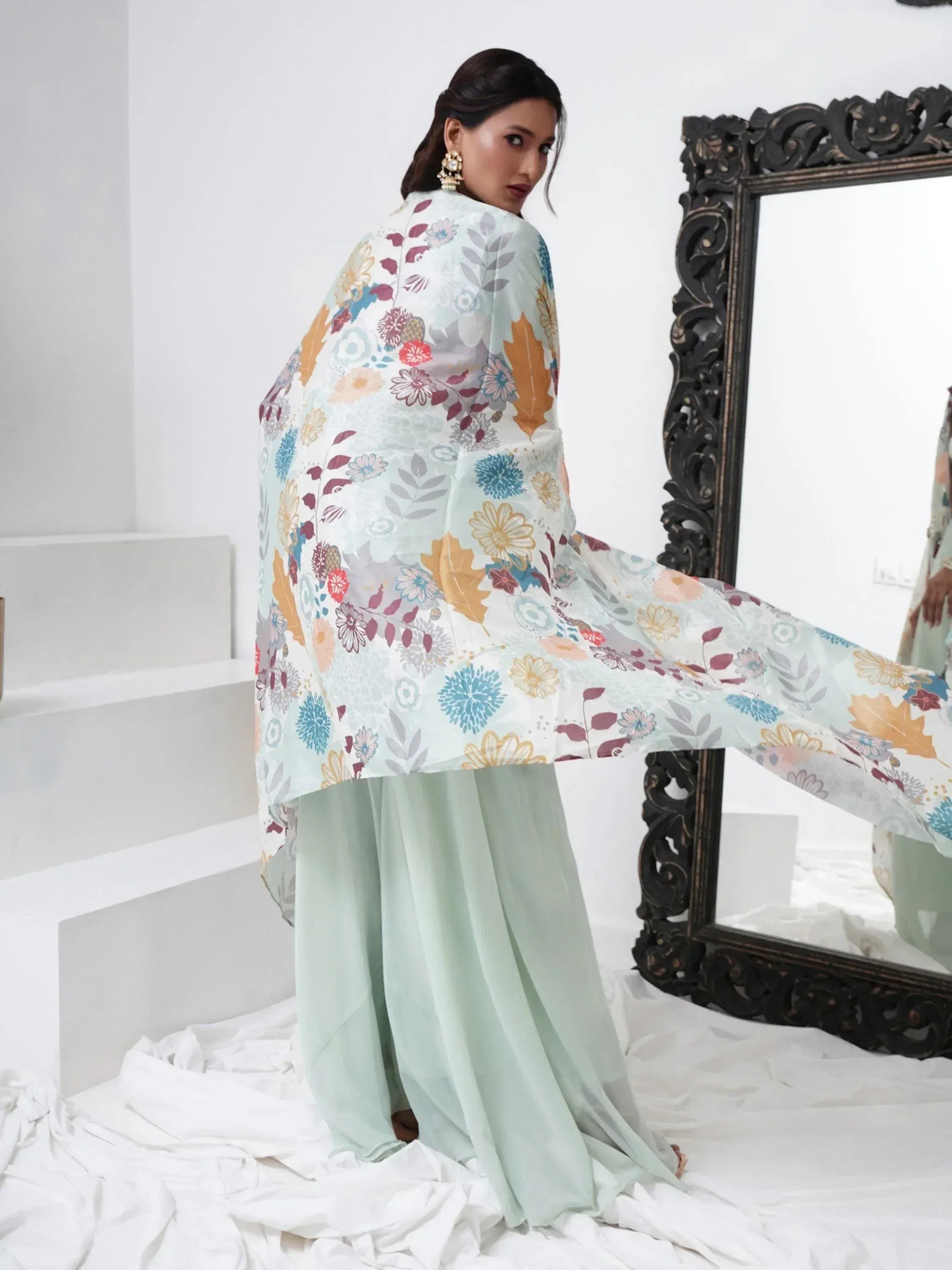 Woman in light green palazzo suit with multicolor floral dupatta, standing by mirror