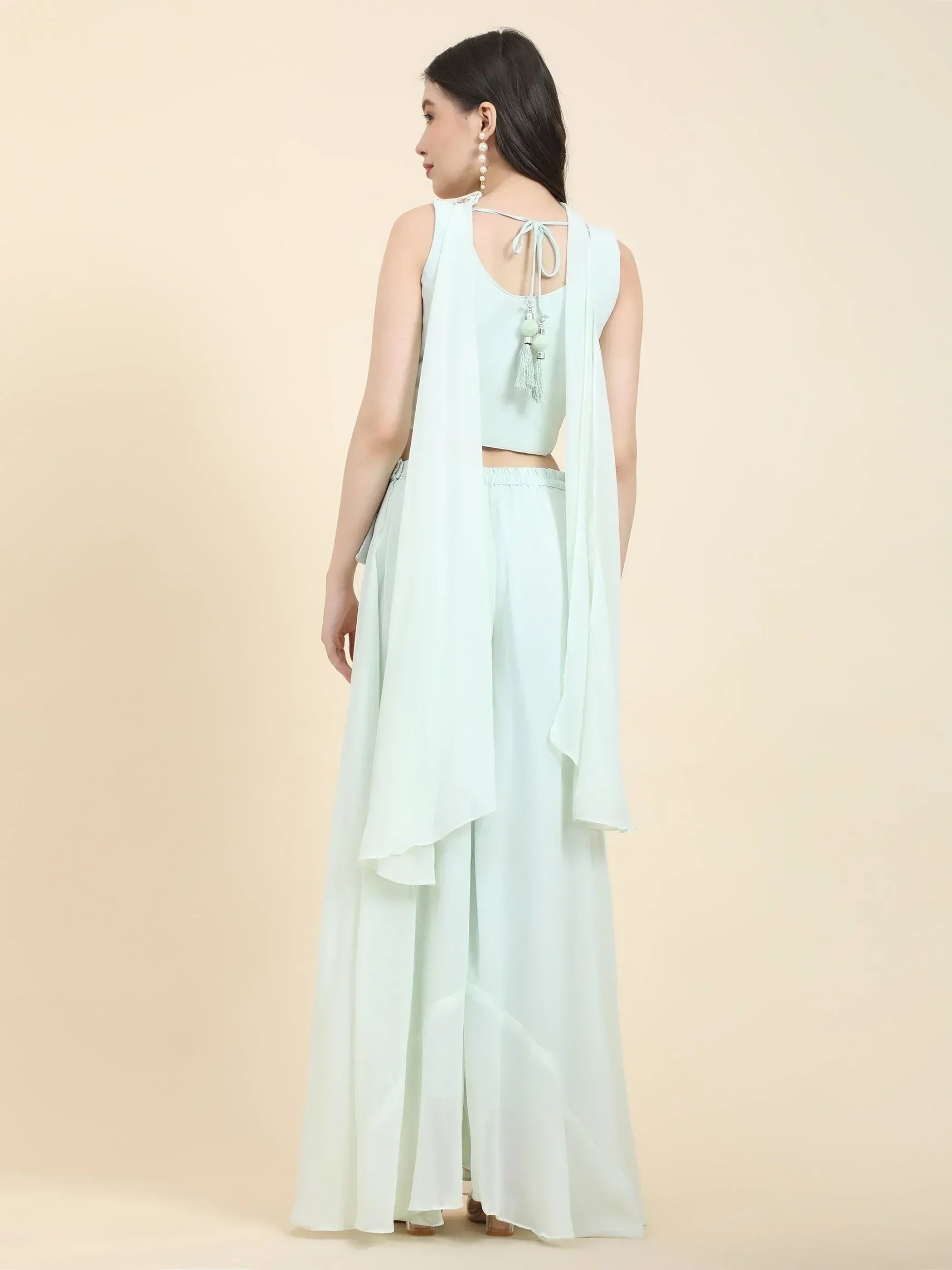 Woman wearing light pastel green ethnic palazzo set with sleeveless top, back tassel detail.