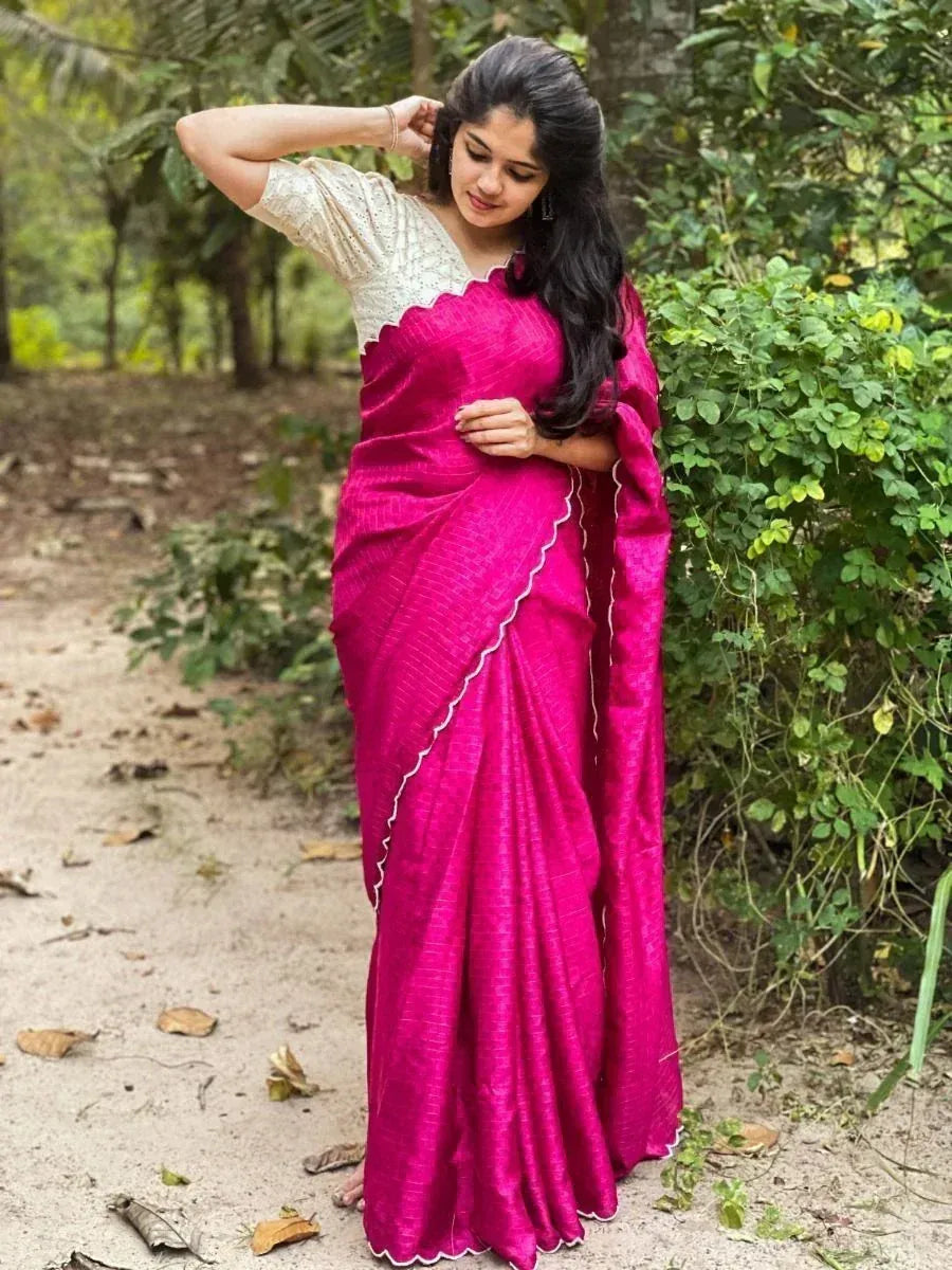 Woman in vibrant pink saree with scalloped white border, paired with embroidered blouse, outdoors
