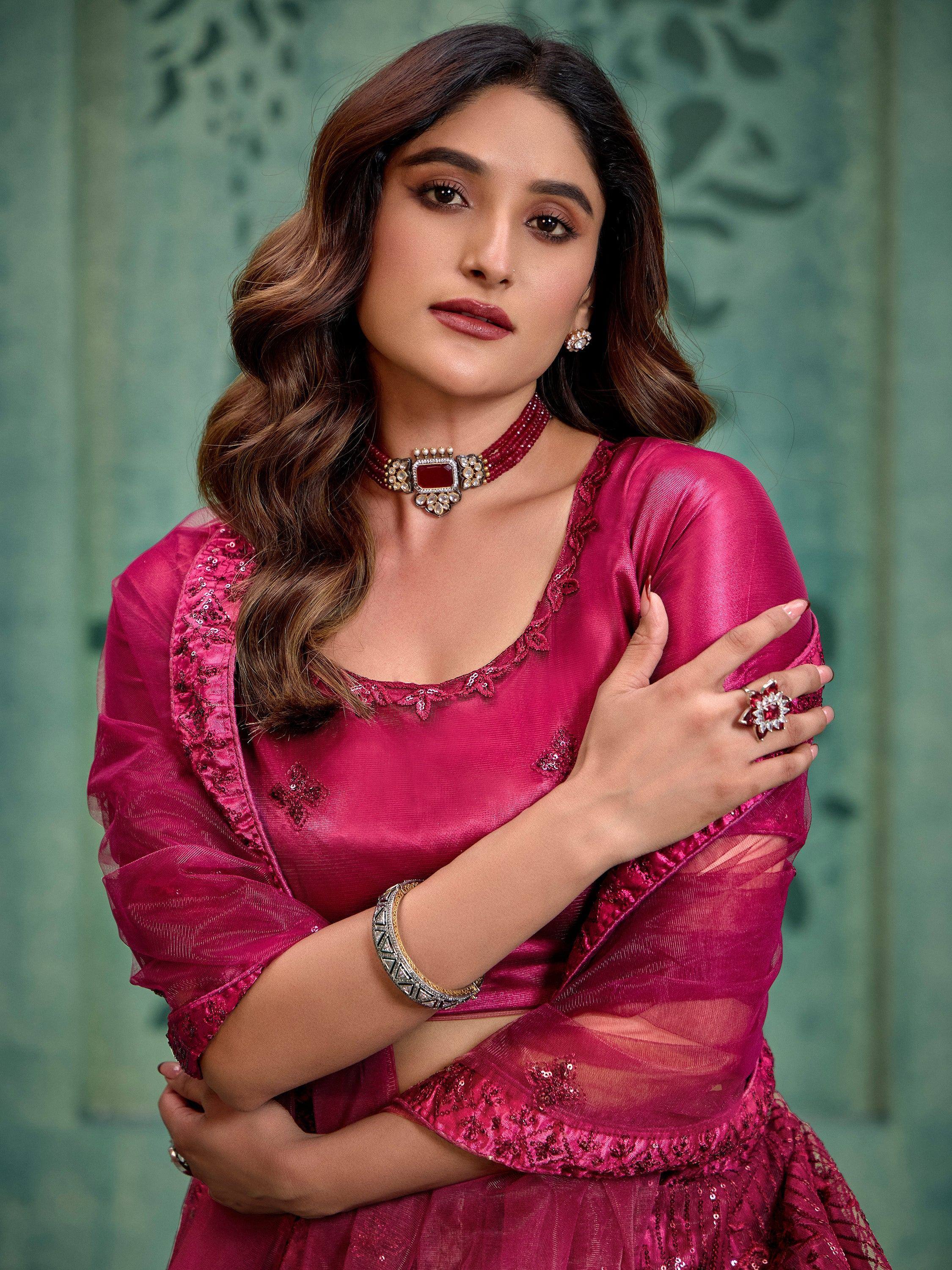 Woman in pink ethnic gown with sequin embroidery, statement jewelry, and sheer overlay for festive occasions