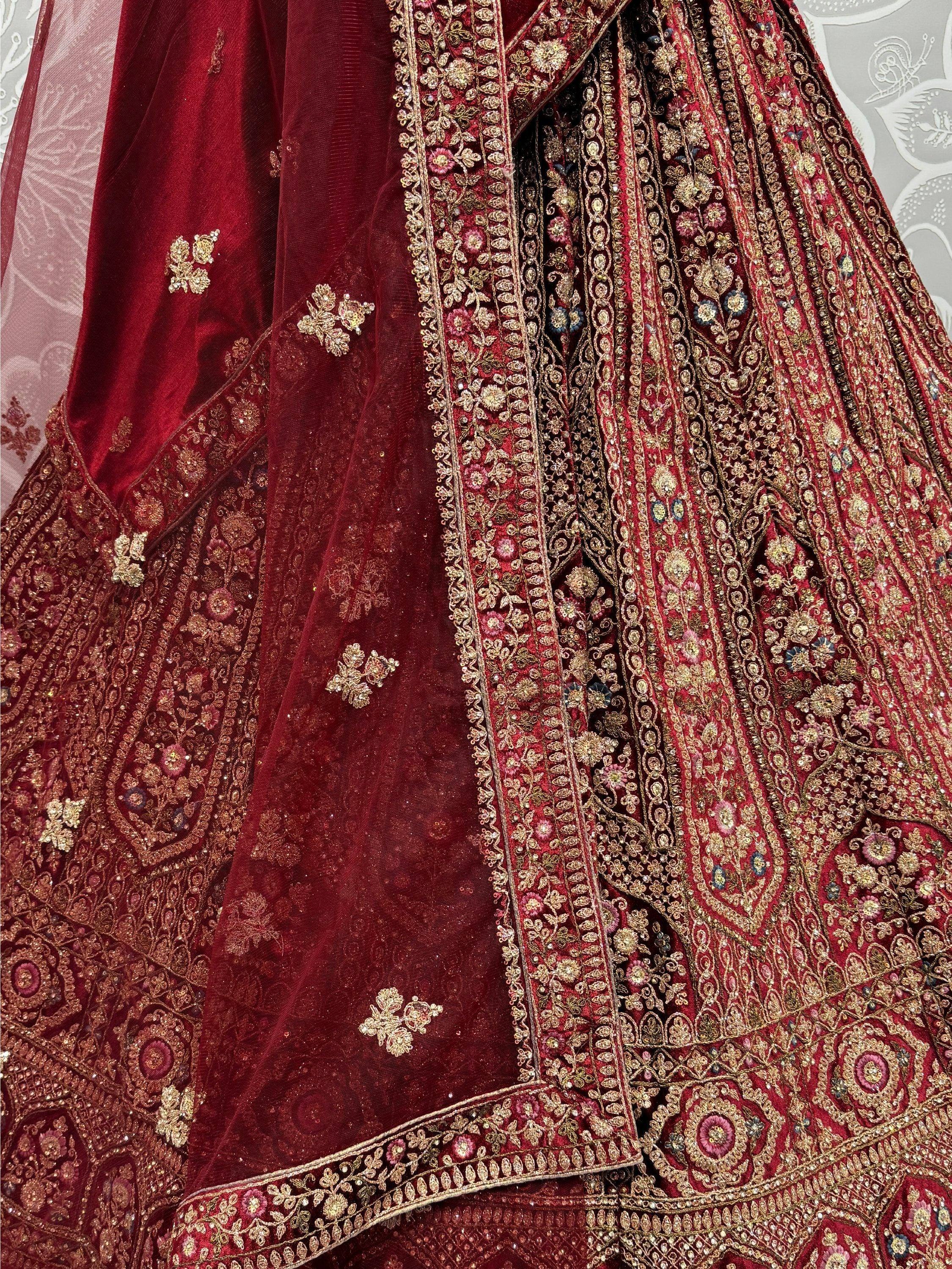 Luxury maroon velvet lehenga choli with intricate gold embroidery and floral zari work, perfect for Indian weddings.