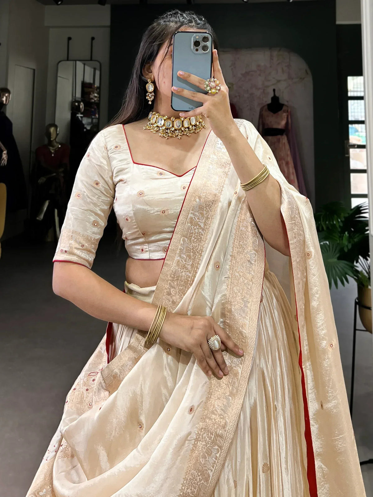 Cream designer lehenga choli with red trim, traditional Indian ethnic wear, paired with gold jewelry