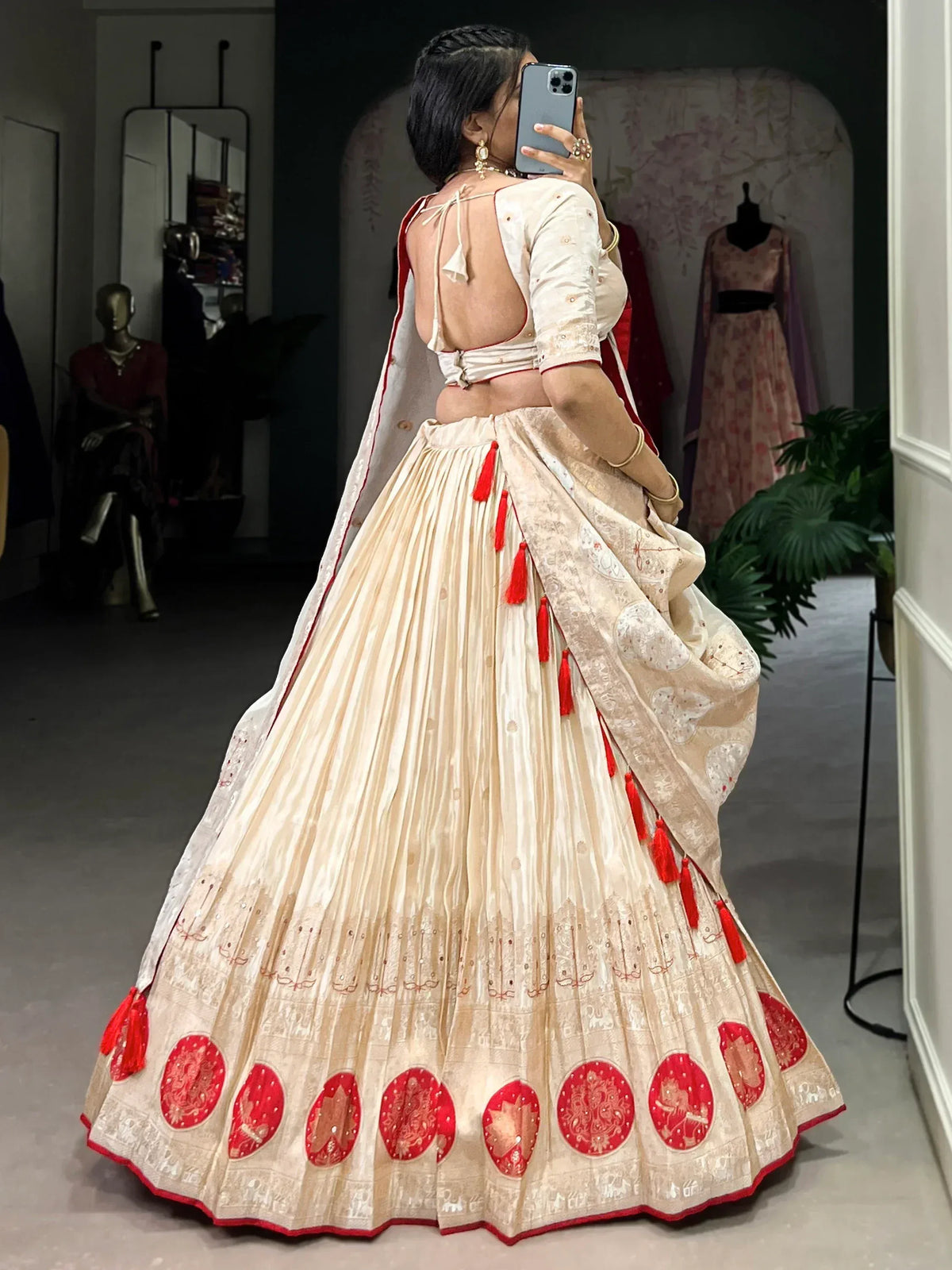 Cream and red designer lehenga choli with backless blouse, tassels, and embroidered motifs, perfect for Indian weddings.