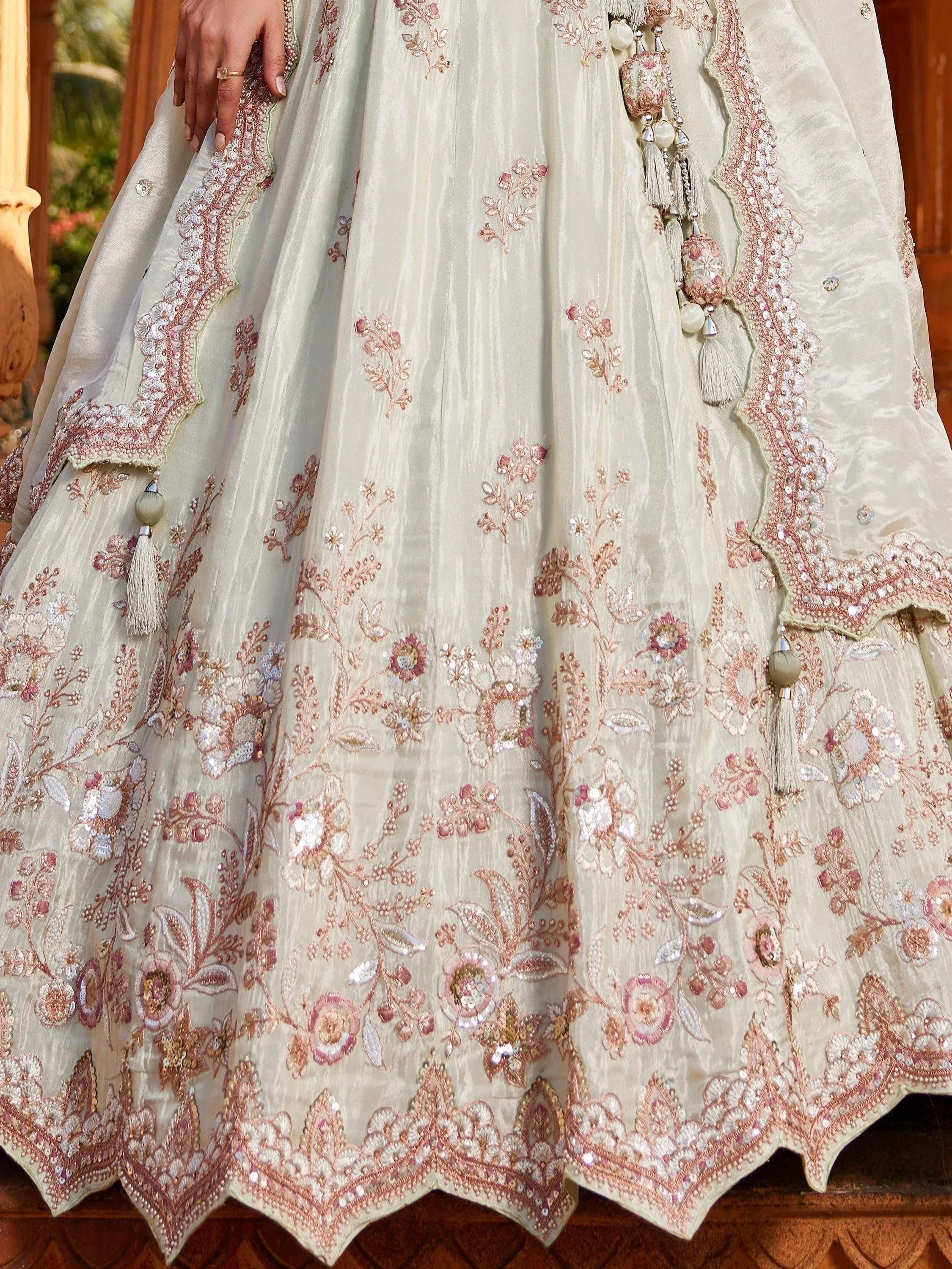 Elegant cream lehenga with pink floral embroidery and tassels, perfect for Indian weddings and festive occasions.
