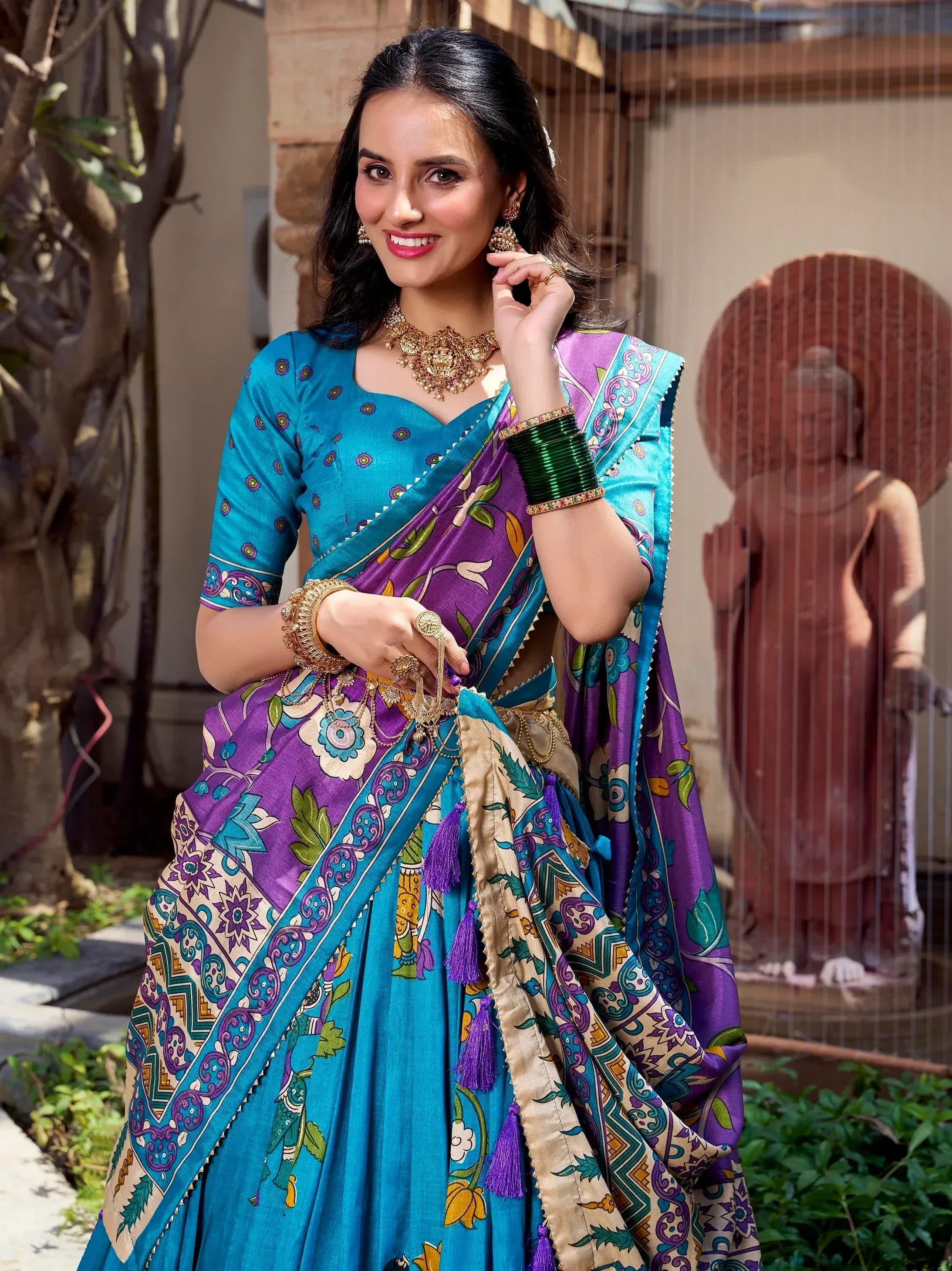 Woman in vibrant blue and purple printed saree with gold jewelry, styled for Indian ethnic wear occasions