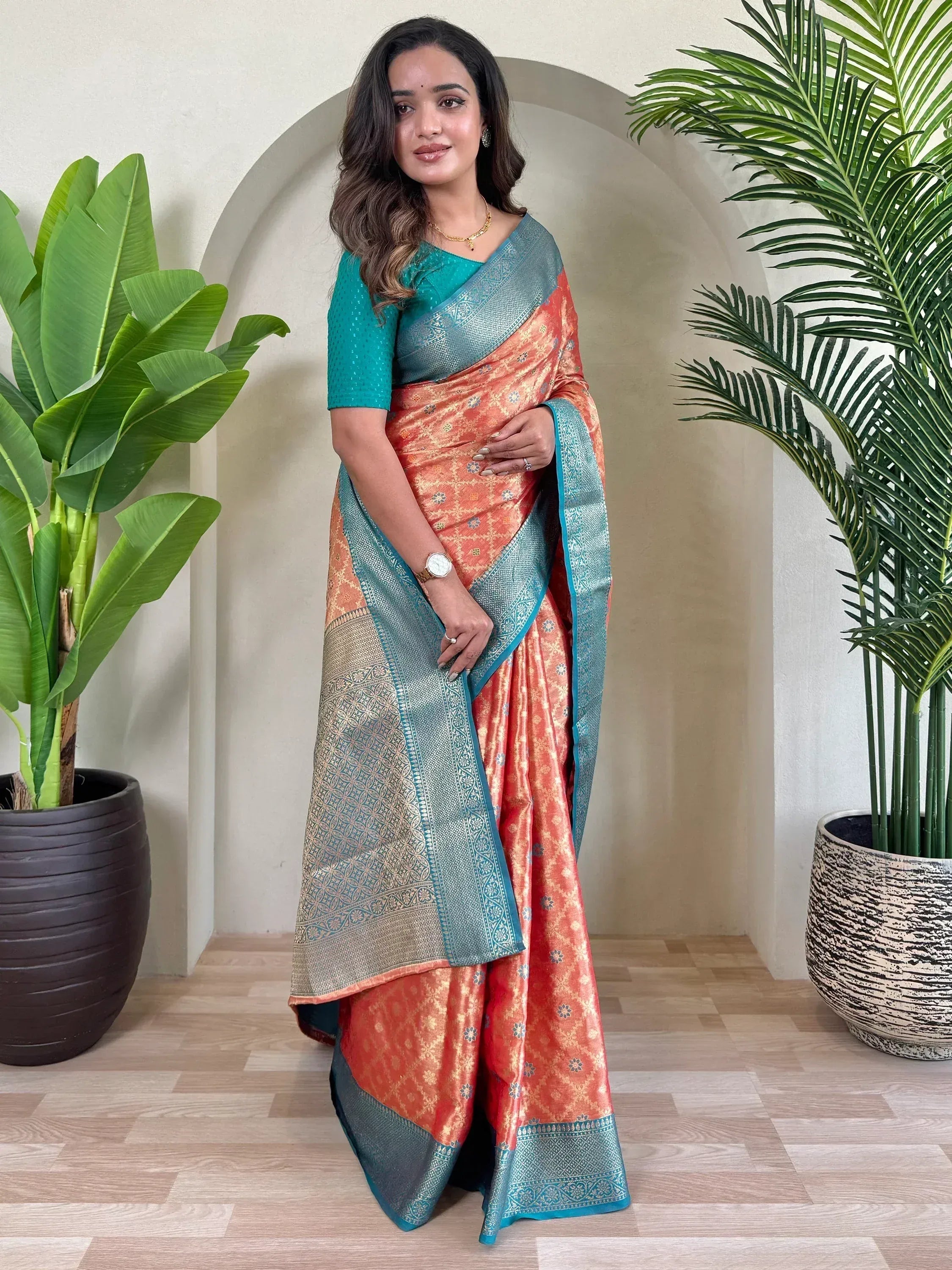 Woman in orange and teal designer saree with gold motifs, styled for ethnic occasions