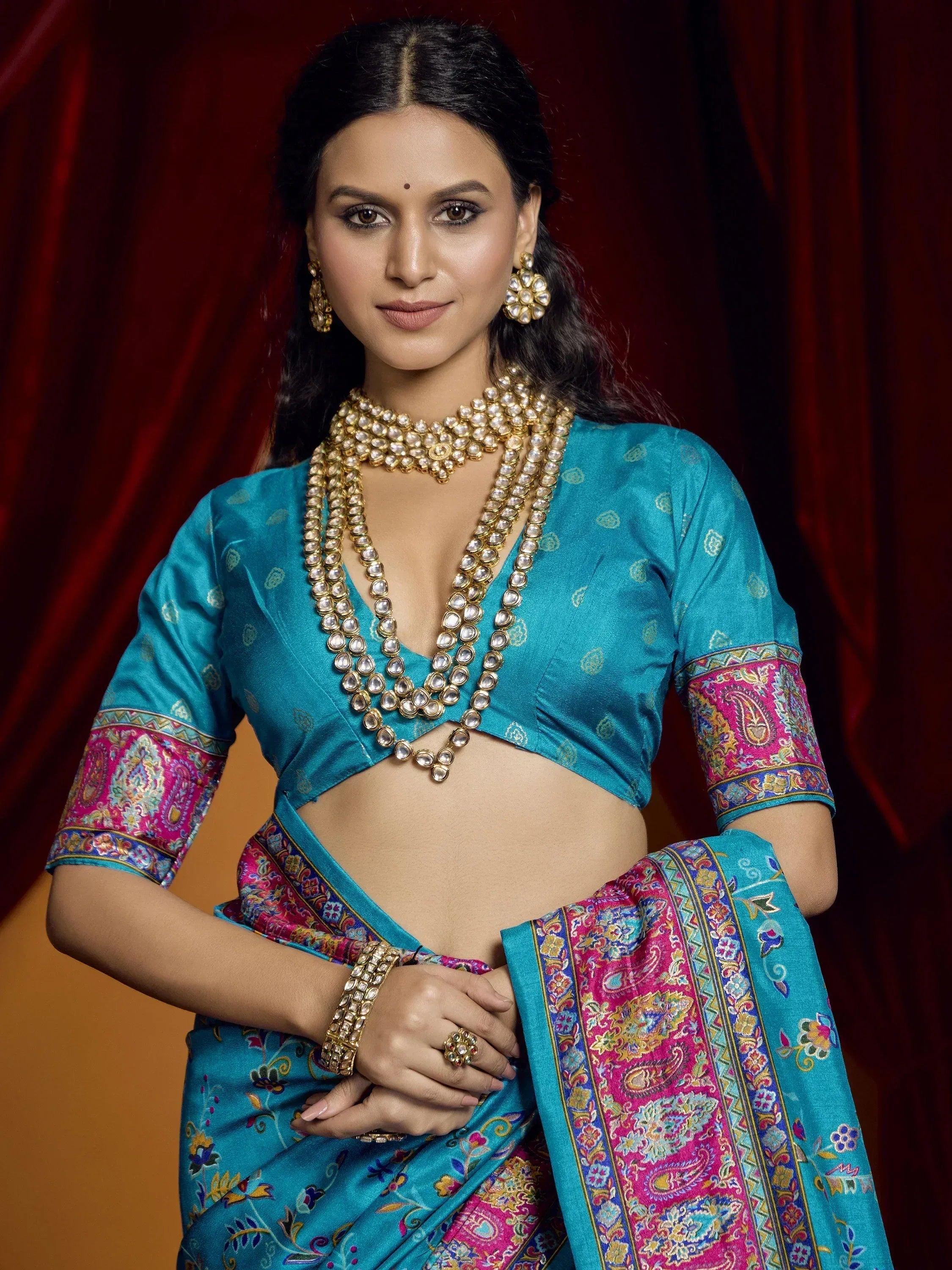 Woman in turquoise Indian saree with pink paisley border, gold jewelry, and designer blouse for ethnic wear