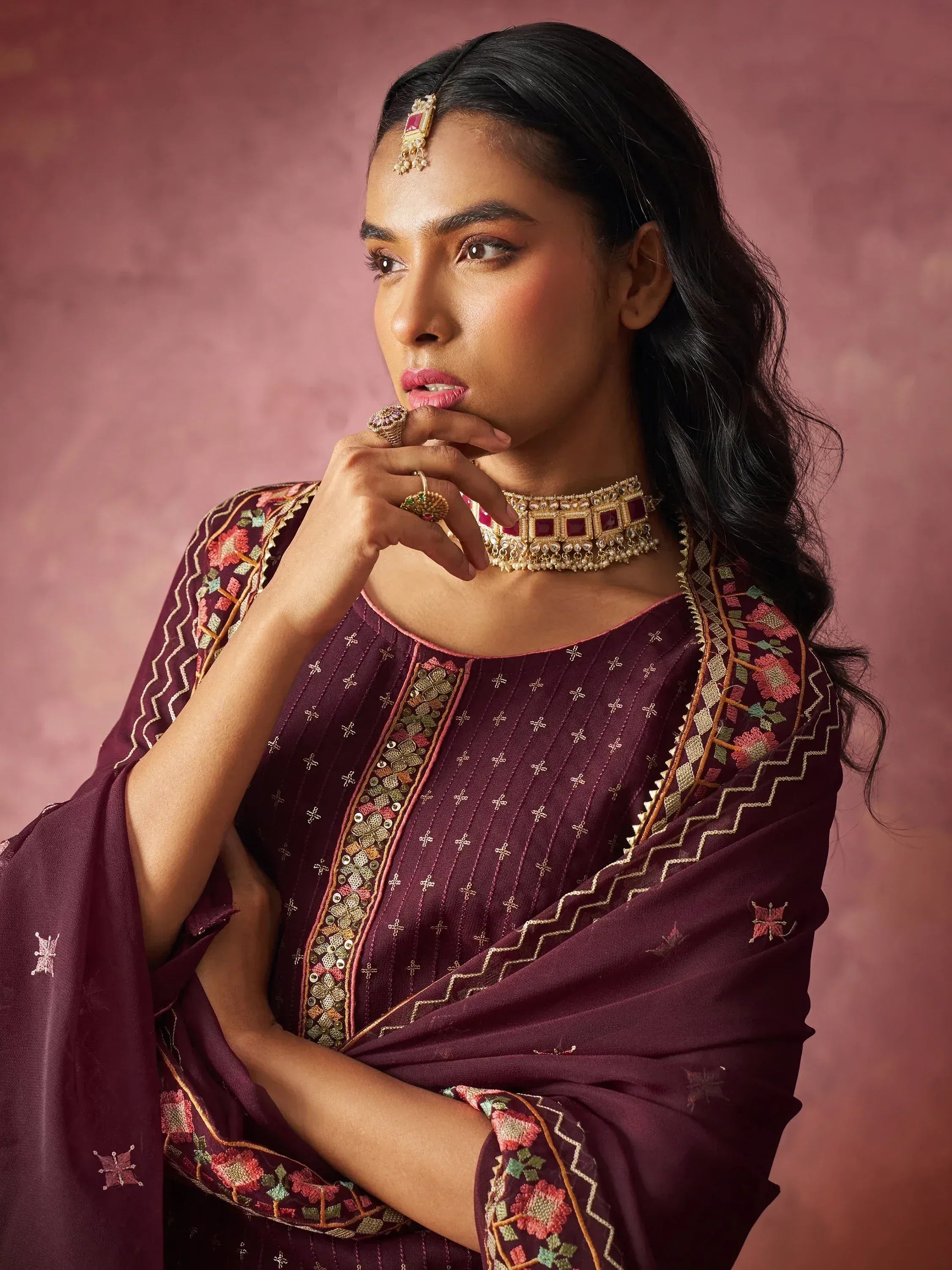 Woman in maroon embroidered ethnic wear with floral patterns and traditional jewelry