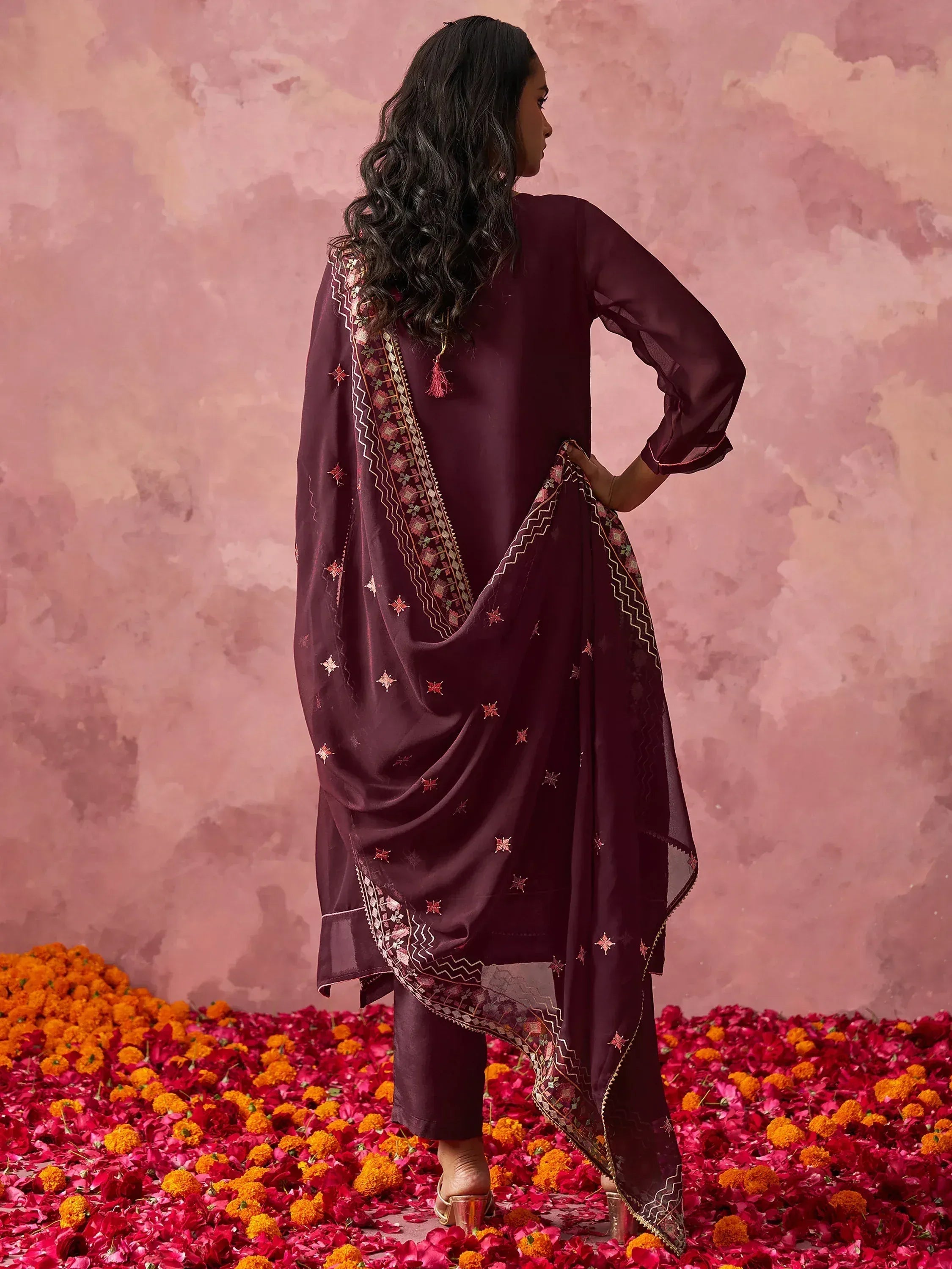 Elegant maroon salwar kameez with embroidered dupatta, styled for festive occasions amidst floral petals.