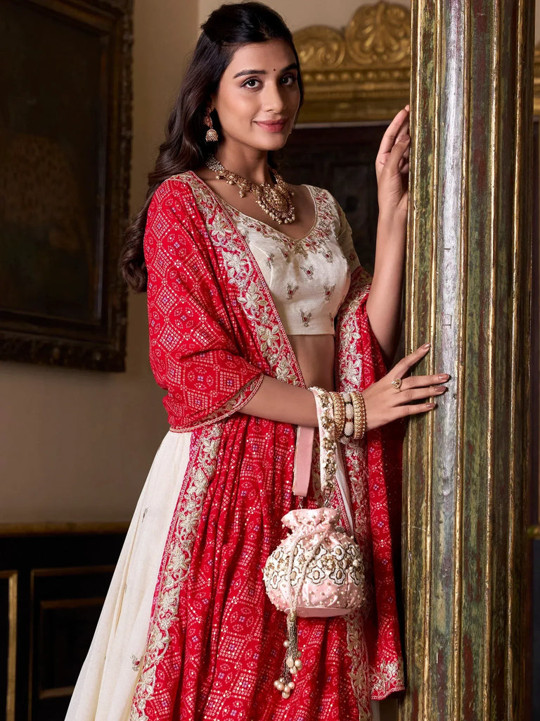 Red and ivory embroidered lehenga choli with gold jewelry and pink potli bag, perfect for Indian weddings and festive occasions.