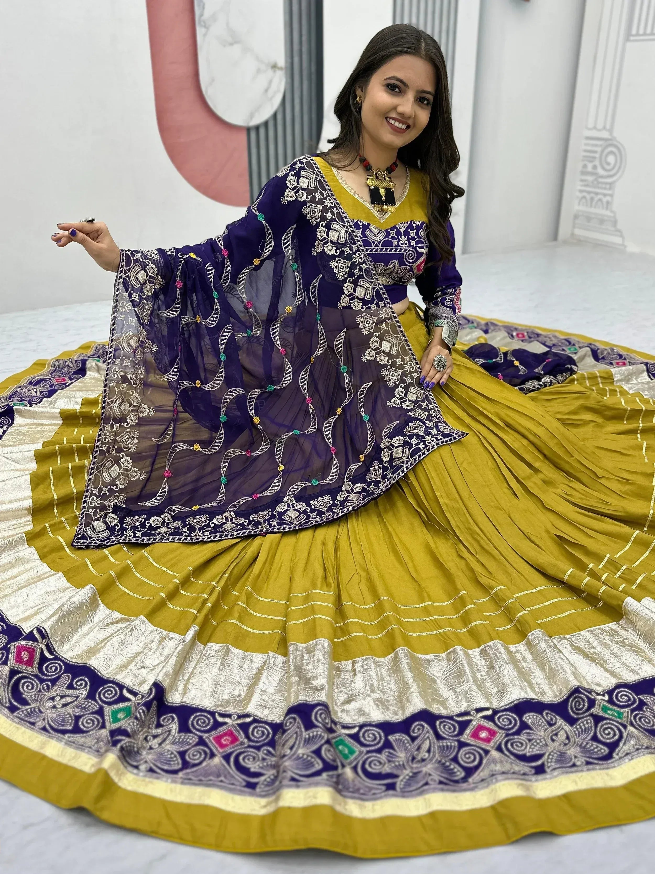 Woman in purple and mustard yellow embroidered lehenga choli with floral dupatta, perfect for Indian ethnic occasions.