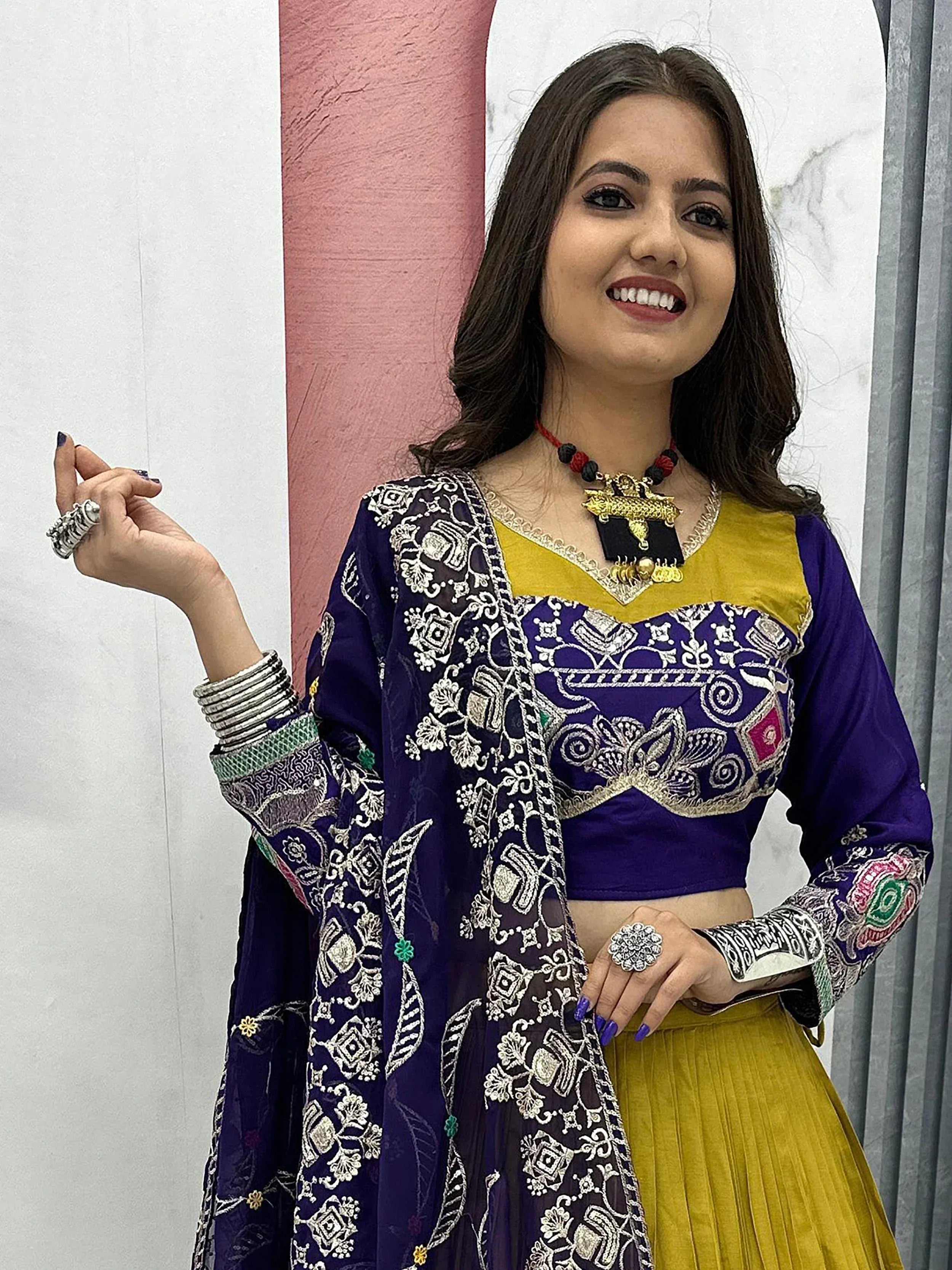 Woman in purple and yellow embroidered ethnic wear with traditional jewelry, perfect for festive occasions.