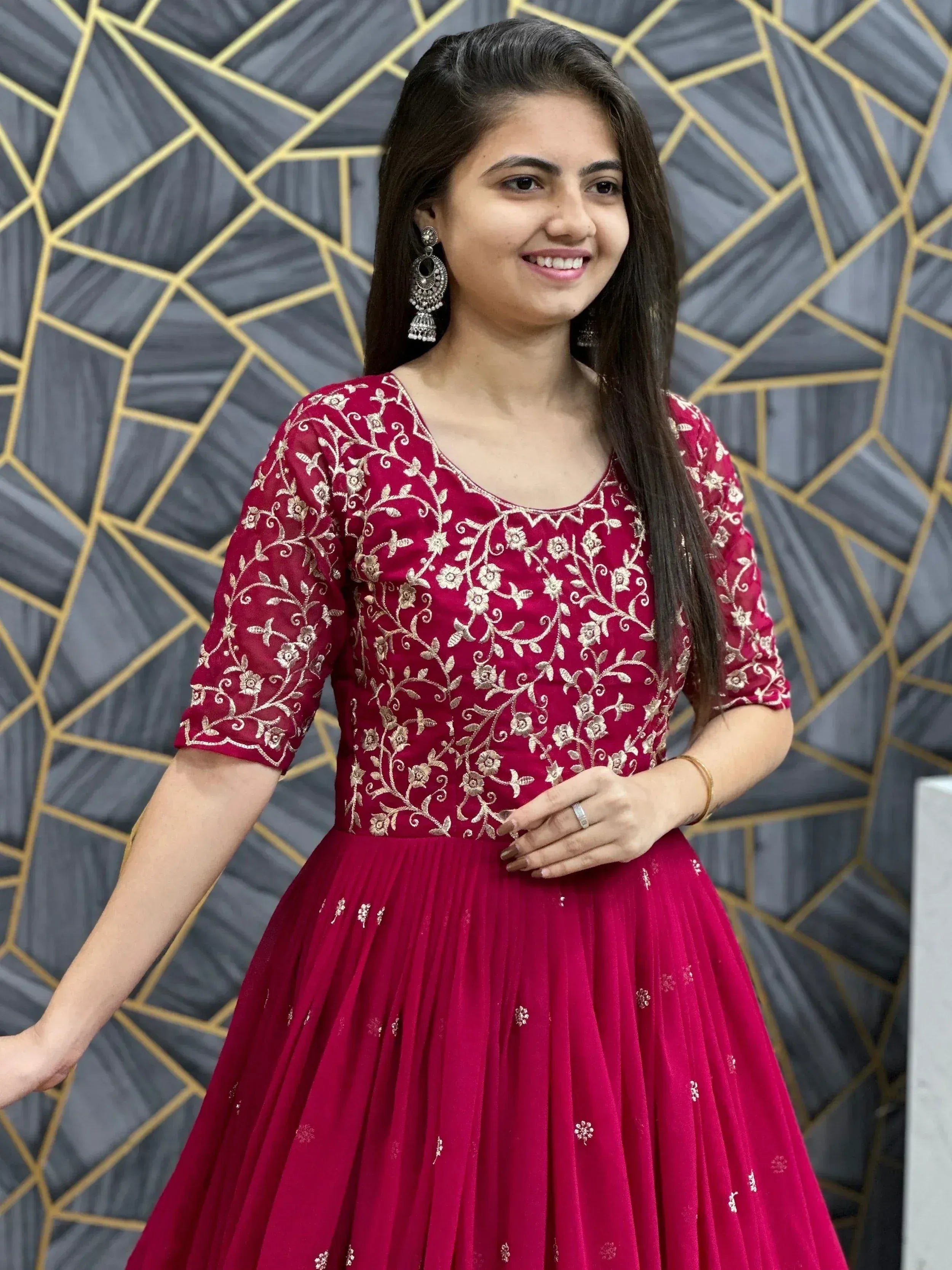 Woman in maroon ethnic gown with gold floral embroidery, perfect for Indian occasions and festive wear.
