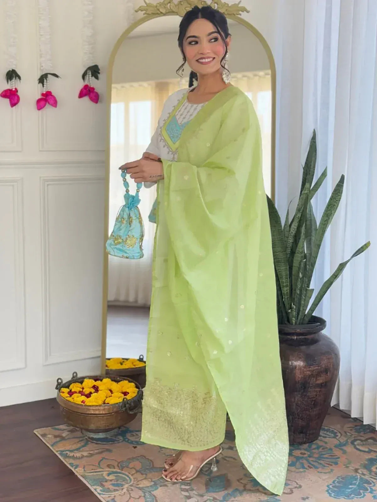 Light green ethnic salwar kameez with embroidery, paired with a blue potli bag for festive occasions.