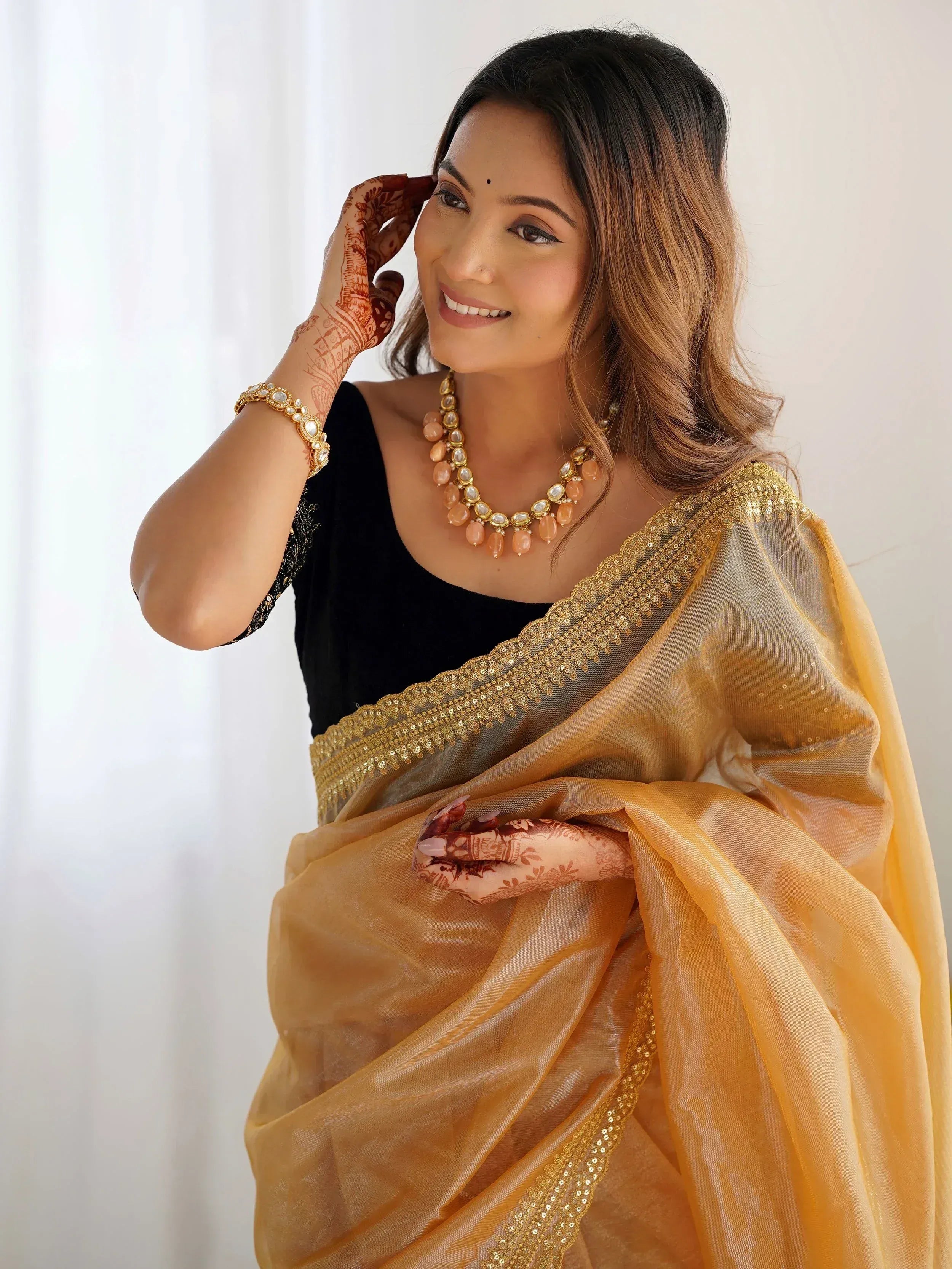 Woman in golden saree with black blouse, henna hands, and traditional jewelry for Indian ethnic wear