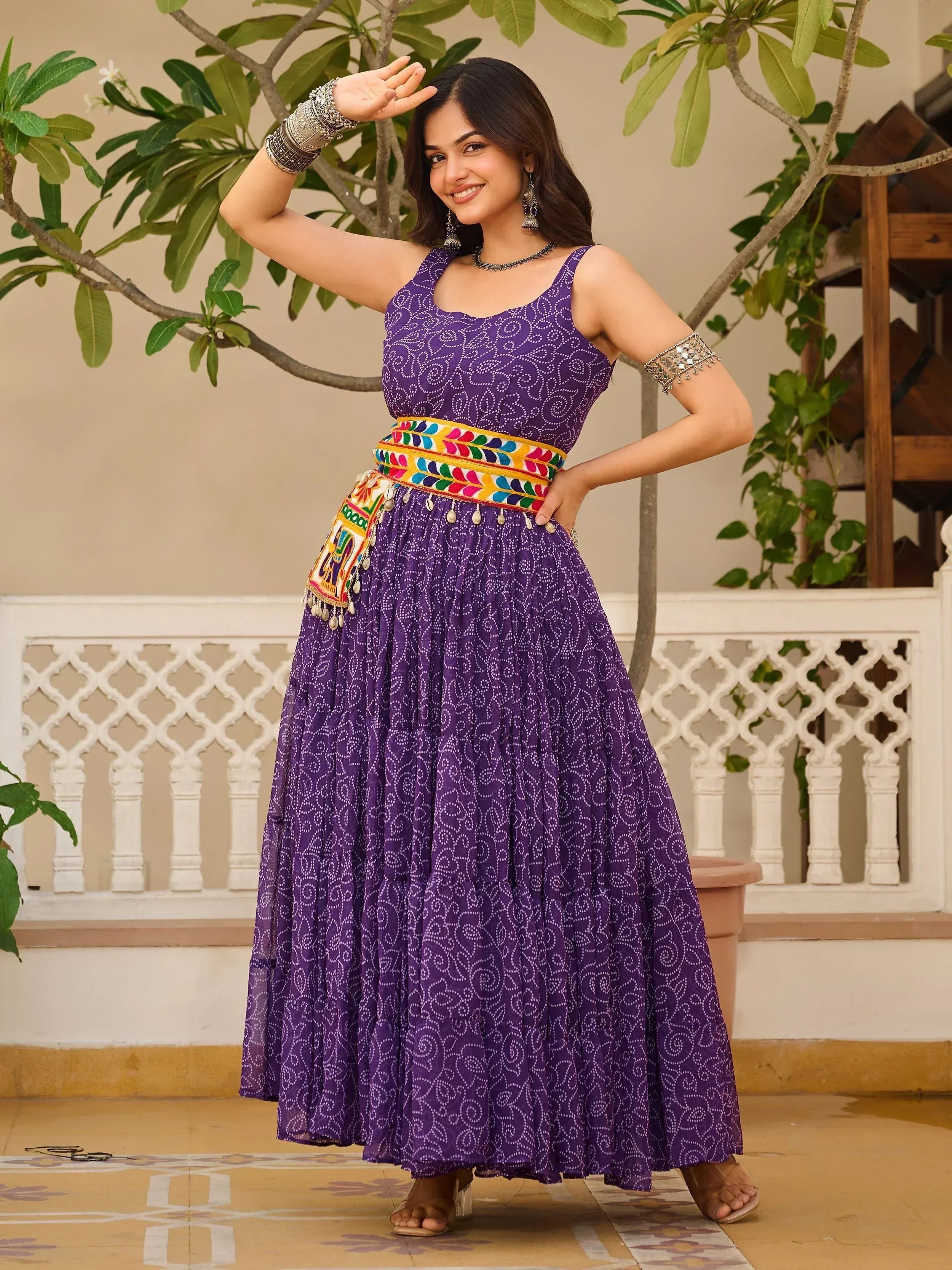 Purple ethnic gown with white swirl print, colorful embroidered belt, and traditional jewelry for Indian wear