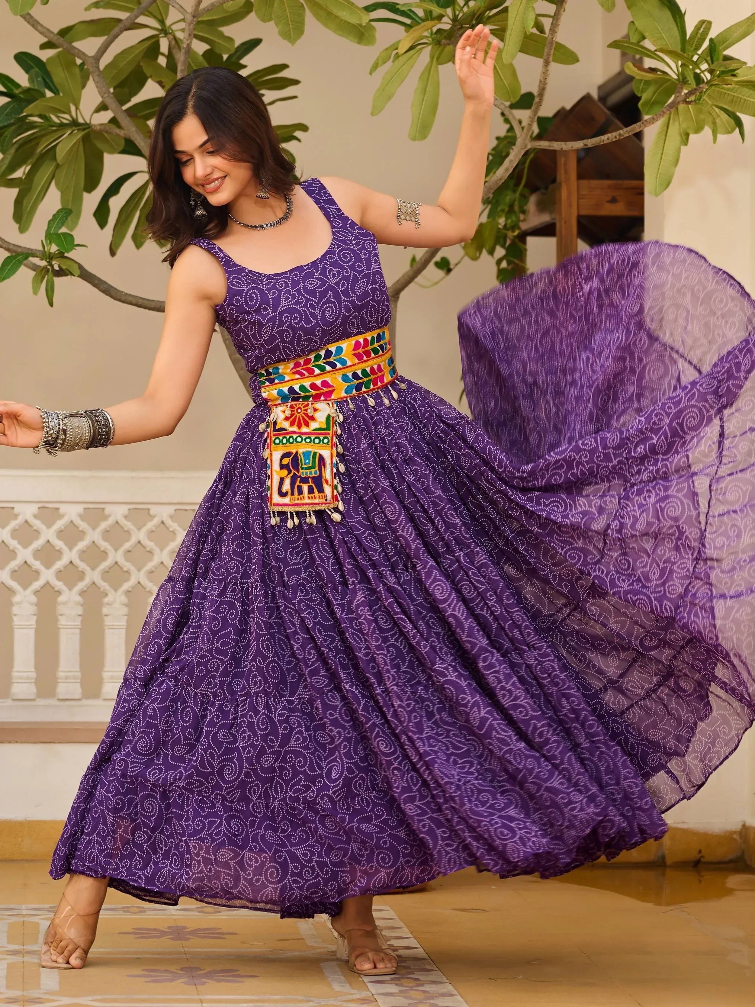 Woman twirling in purple ethnic gown with elephant embroidery, perfect for Indian festive occasions.