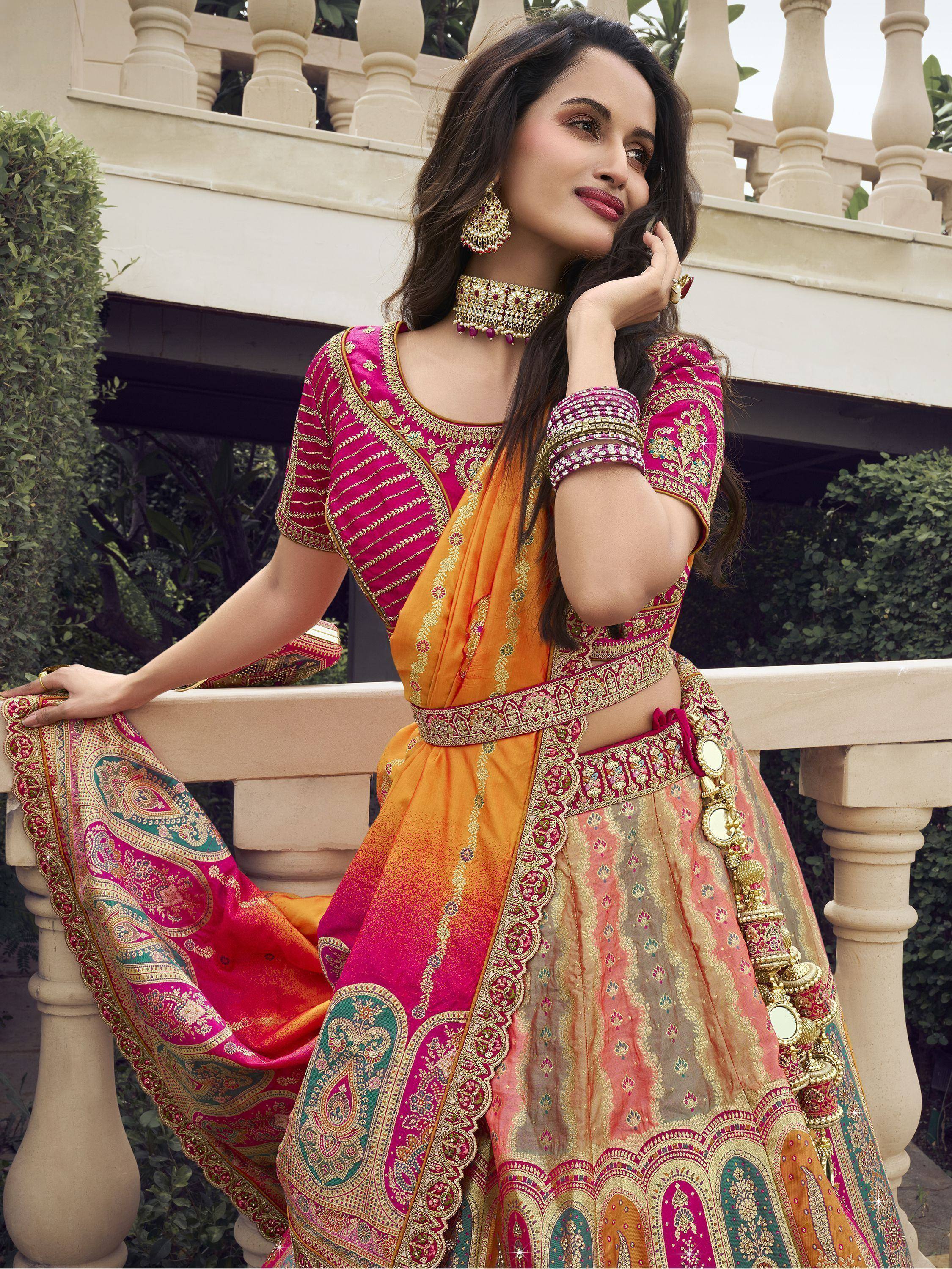 Woman in vibrant pink and orange embroidered lehenga choli with gold detailing, perfect for Indian ethnic occasions.