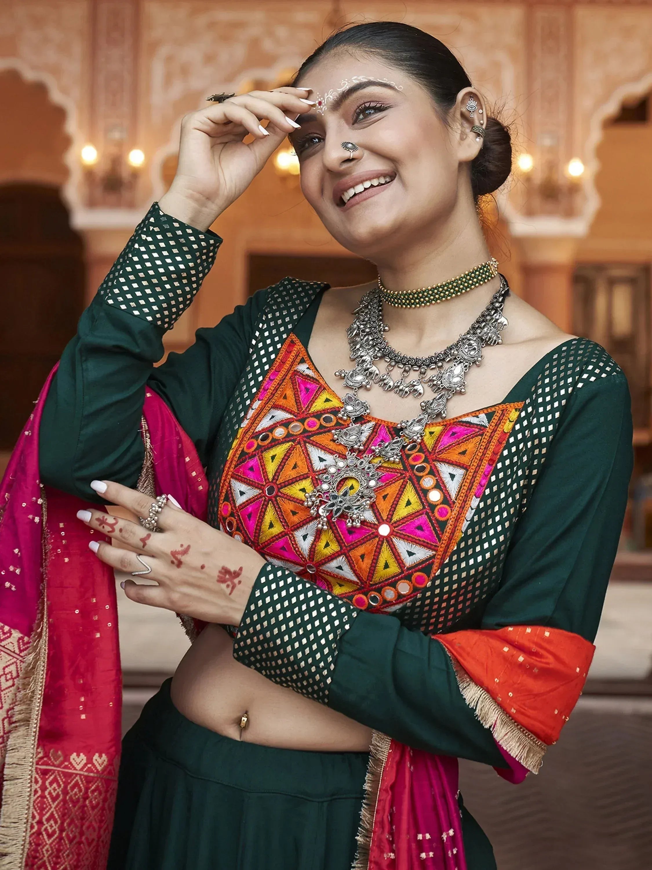 Woman in vibrant green and pink ethnic wear with mirror work, traditional jewelry, and henna, perfect for Indian festivals.