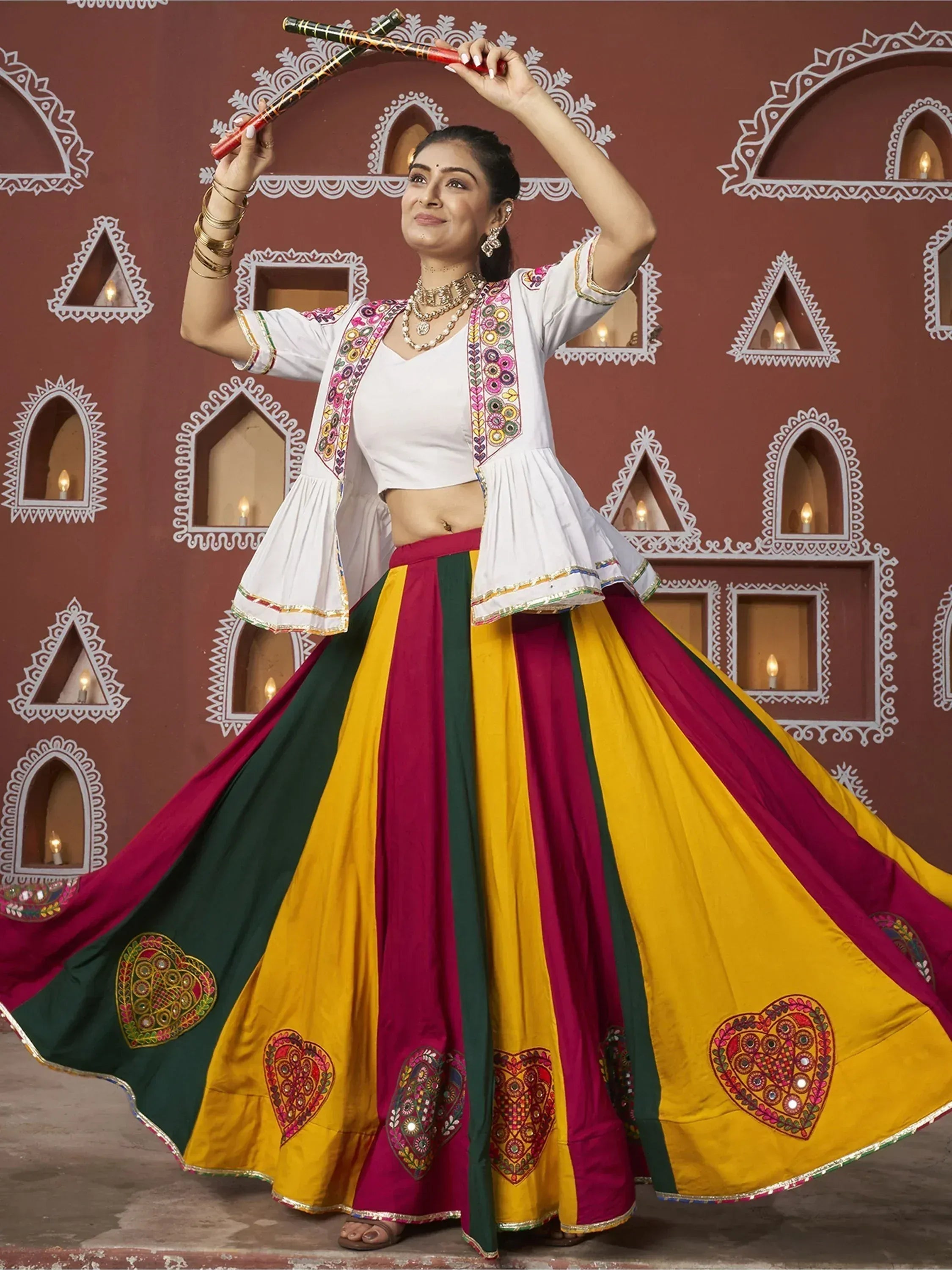 Woman in colorful Indian ethnic wear dancing with dandiya sticks, wearing embroidered white top and striped skirt