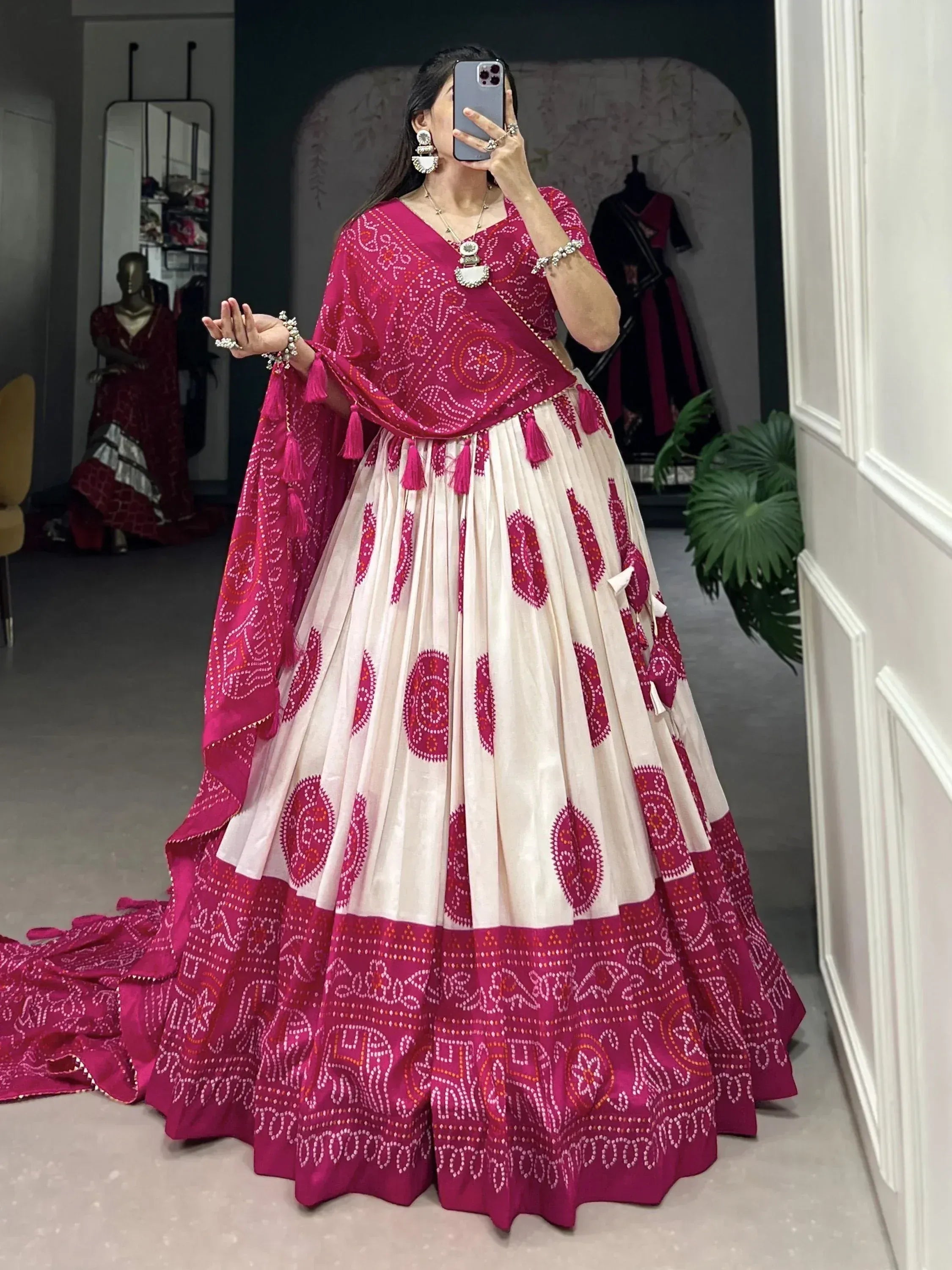 Woman in pink and cream embroidered lehenga choli with tassels, taking mirror selfie in boutique