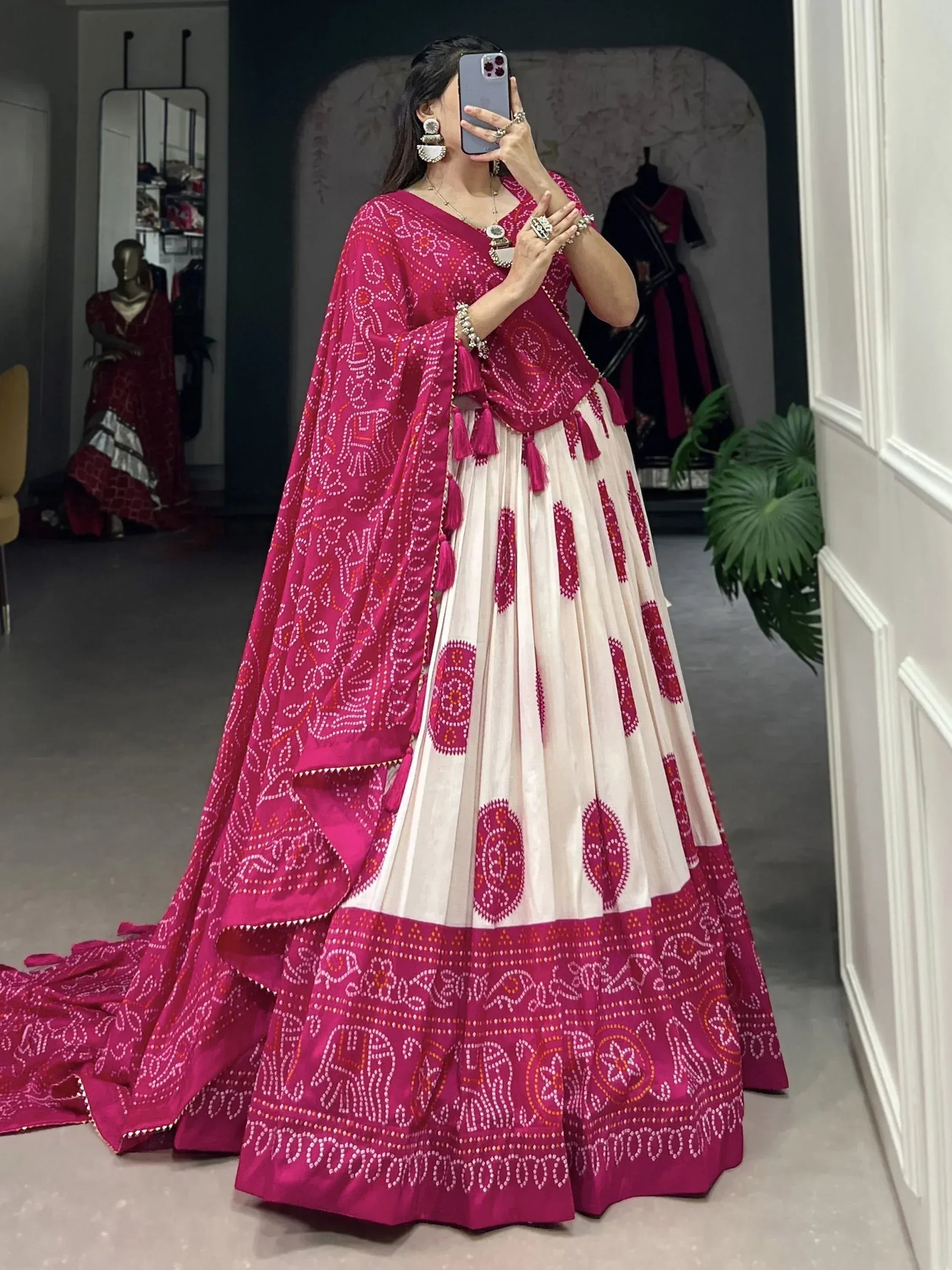 Woman in vibrant pink and cream Bandhani print lehenga choli with tassels, perfect for Indian ethnic wear occasions.