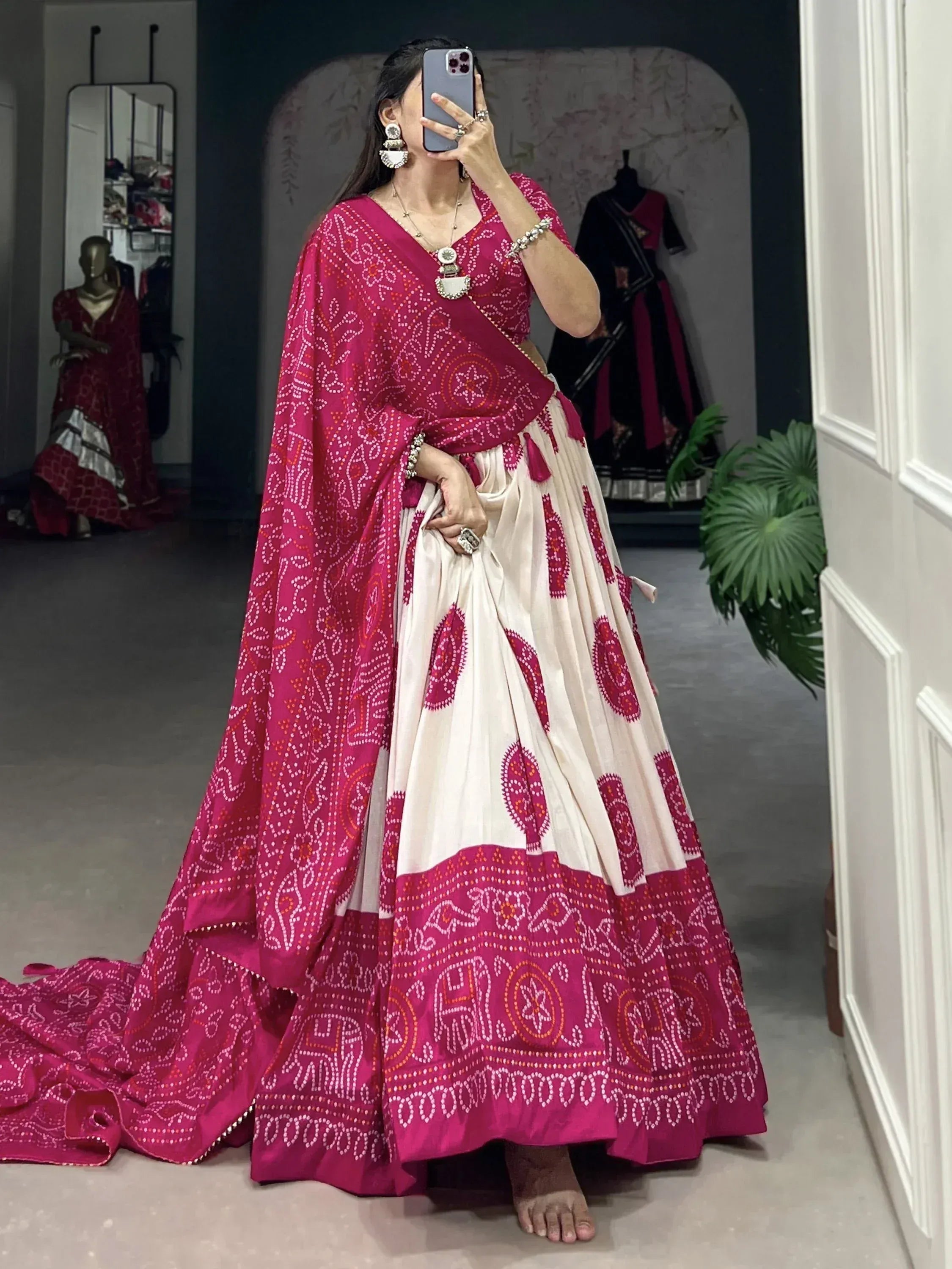 Woman in pink and cream bandhani lehenga choli with mirror work, taking mirror selfie in boutique