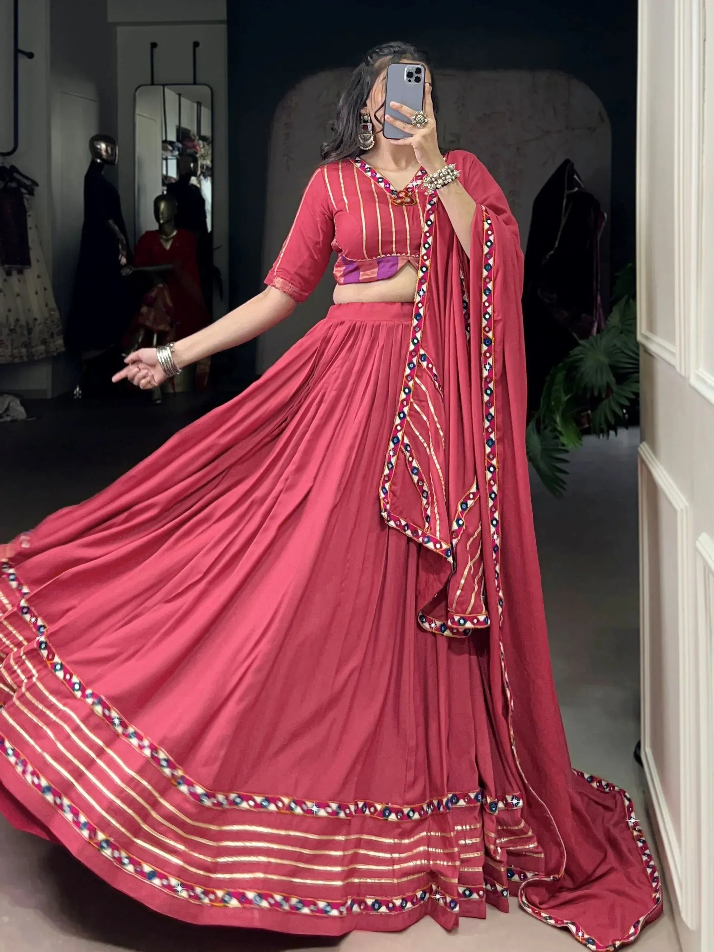 Woman in red ethnic lehenga choli with mirror work, twirling in boutique setting