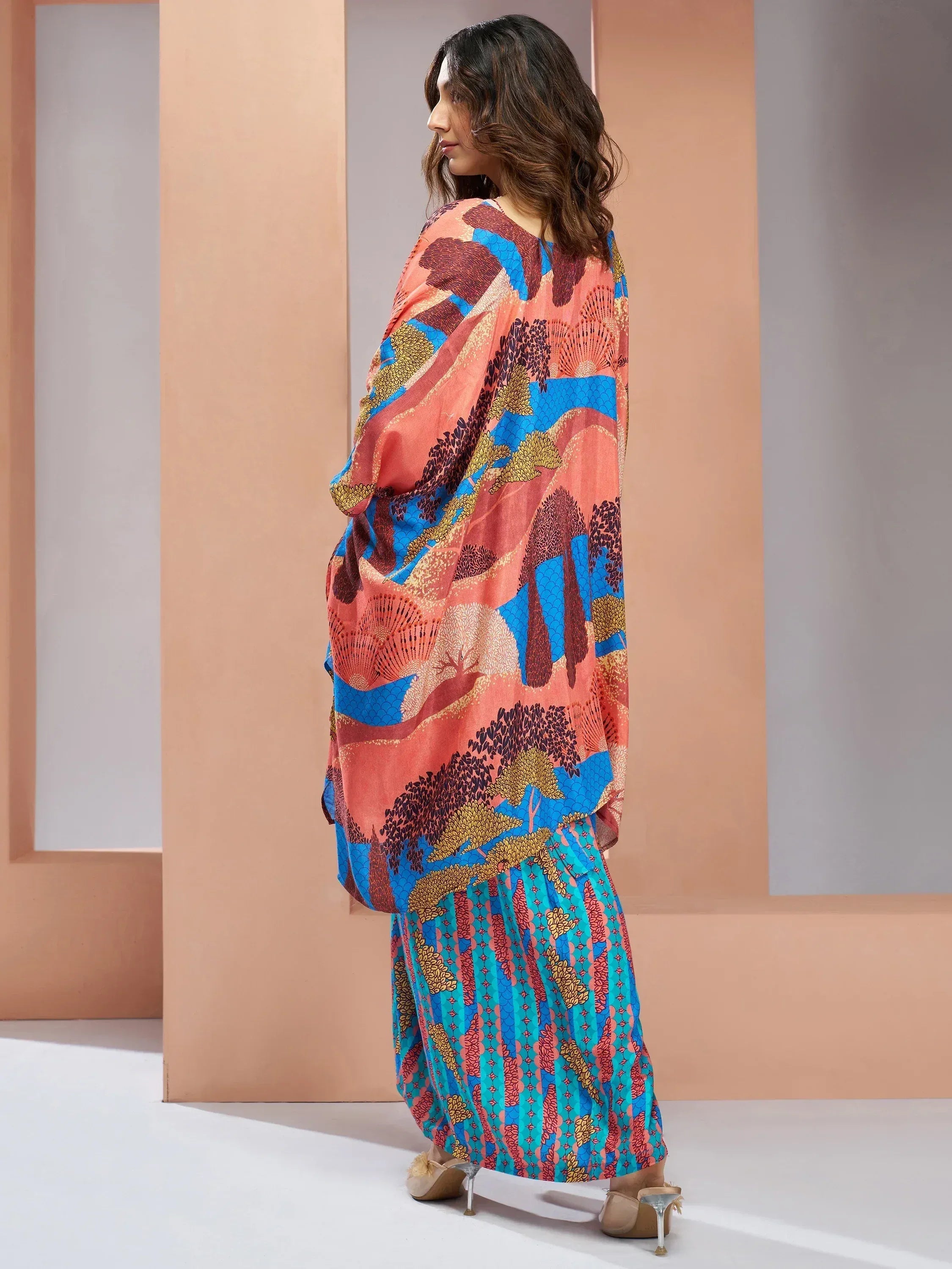 Woman in vibrant printed ethnic gown with floral and landscape motifs, perfect for Indian festive occasions.