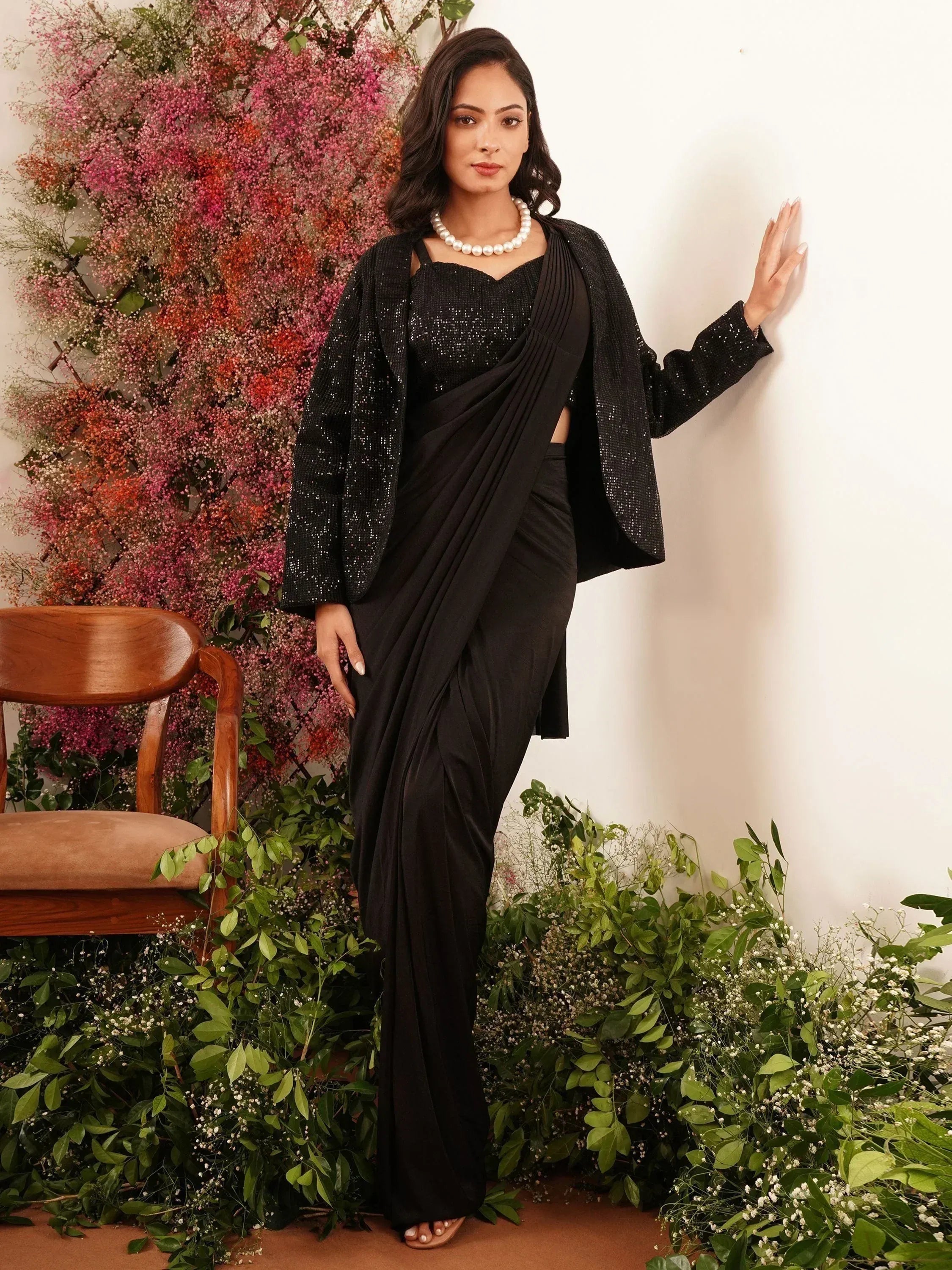 Black sequin saree with matching jacket, styled with pearl necklace against floral backdrop