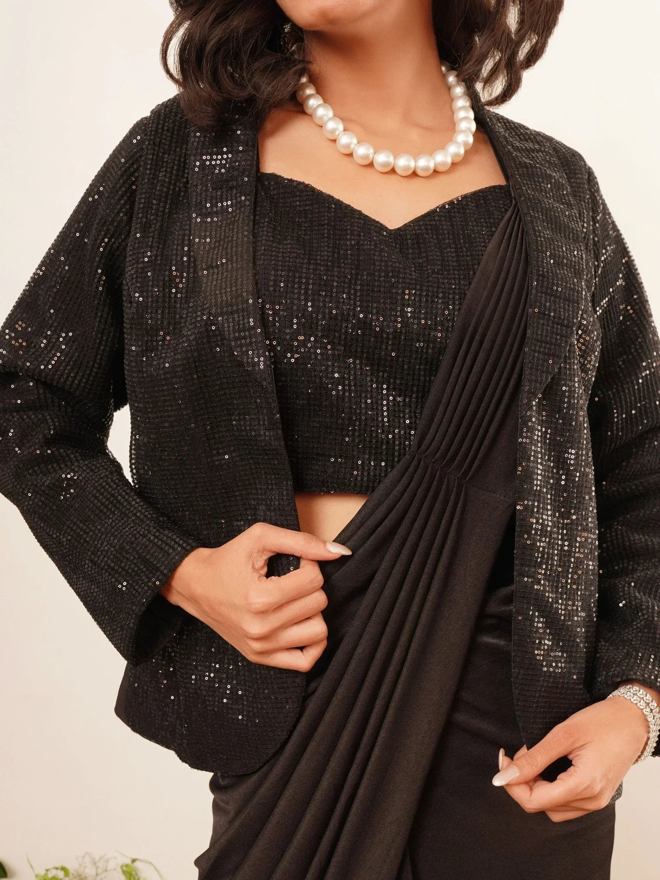 Black sequin saree with pleated drape, pearl necklace, and ethnic blouse for festive occasions