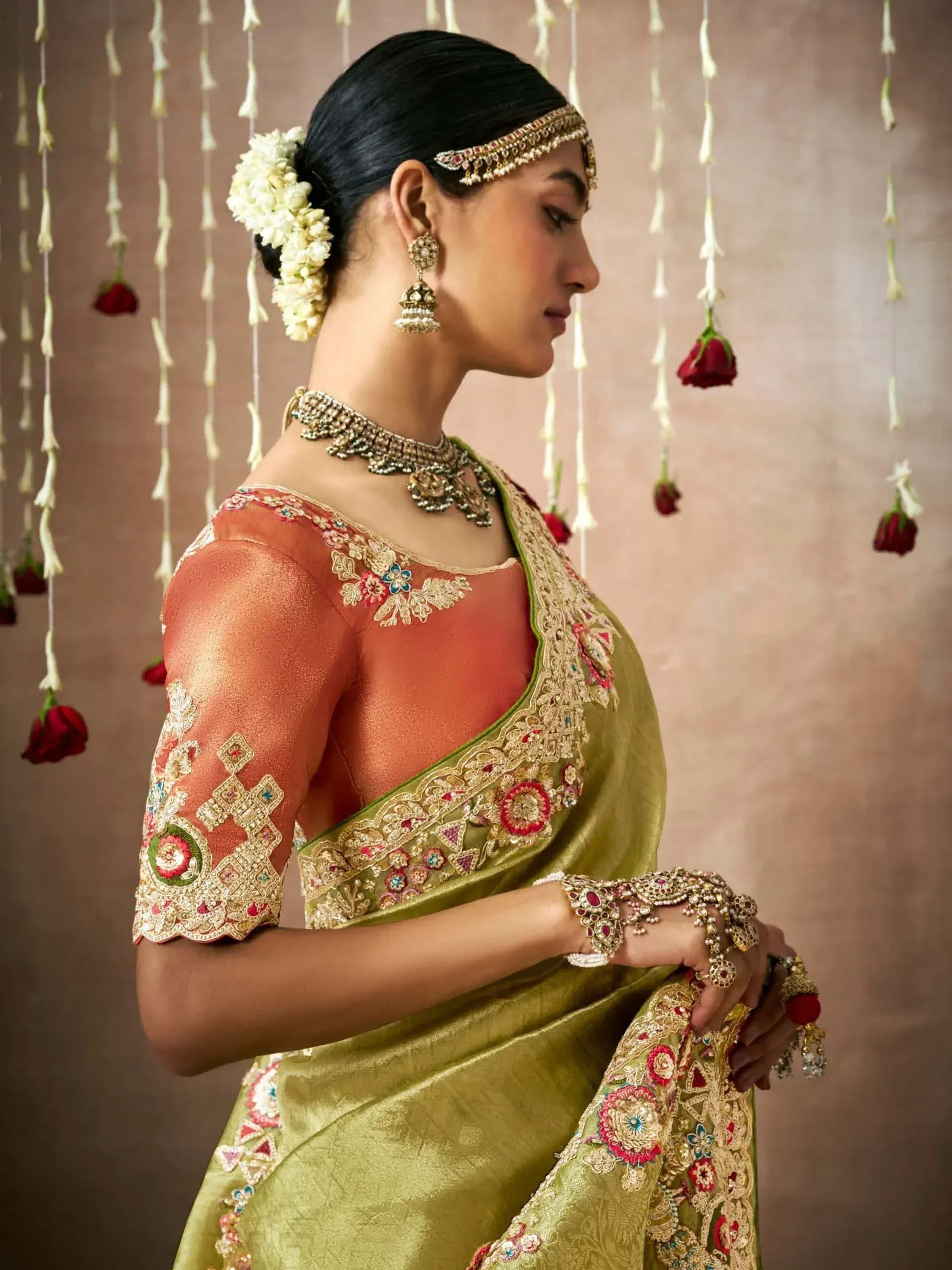 Elegant Indian bride in olive green embroidered saree with peach blouse, traditional jewelry, and floral hair accessories