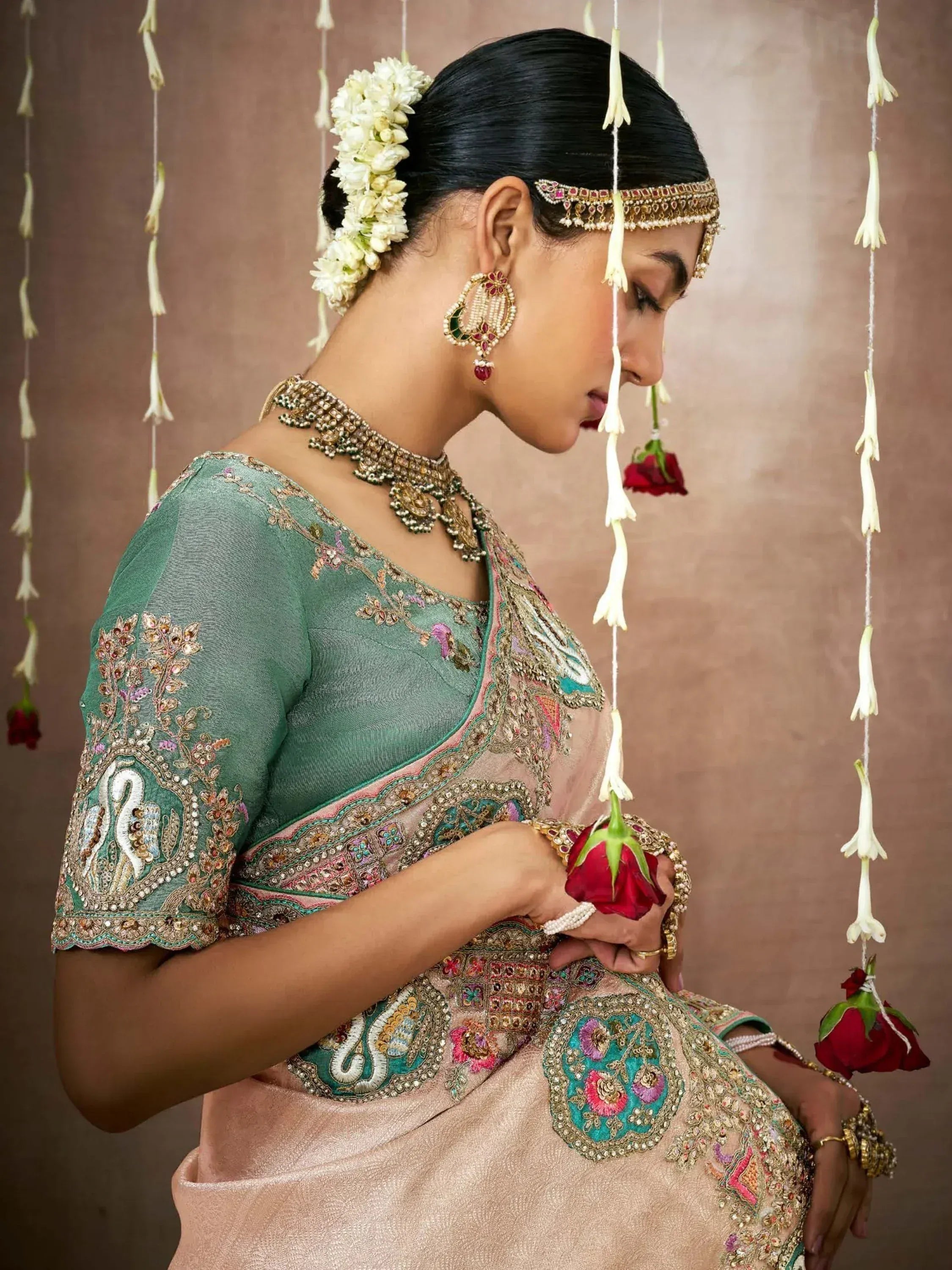 Elegant woman in embroidered green and pink saree with floral hair accessories and traditional jewelry