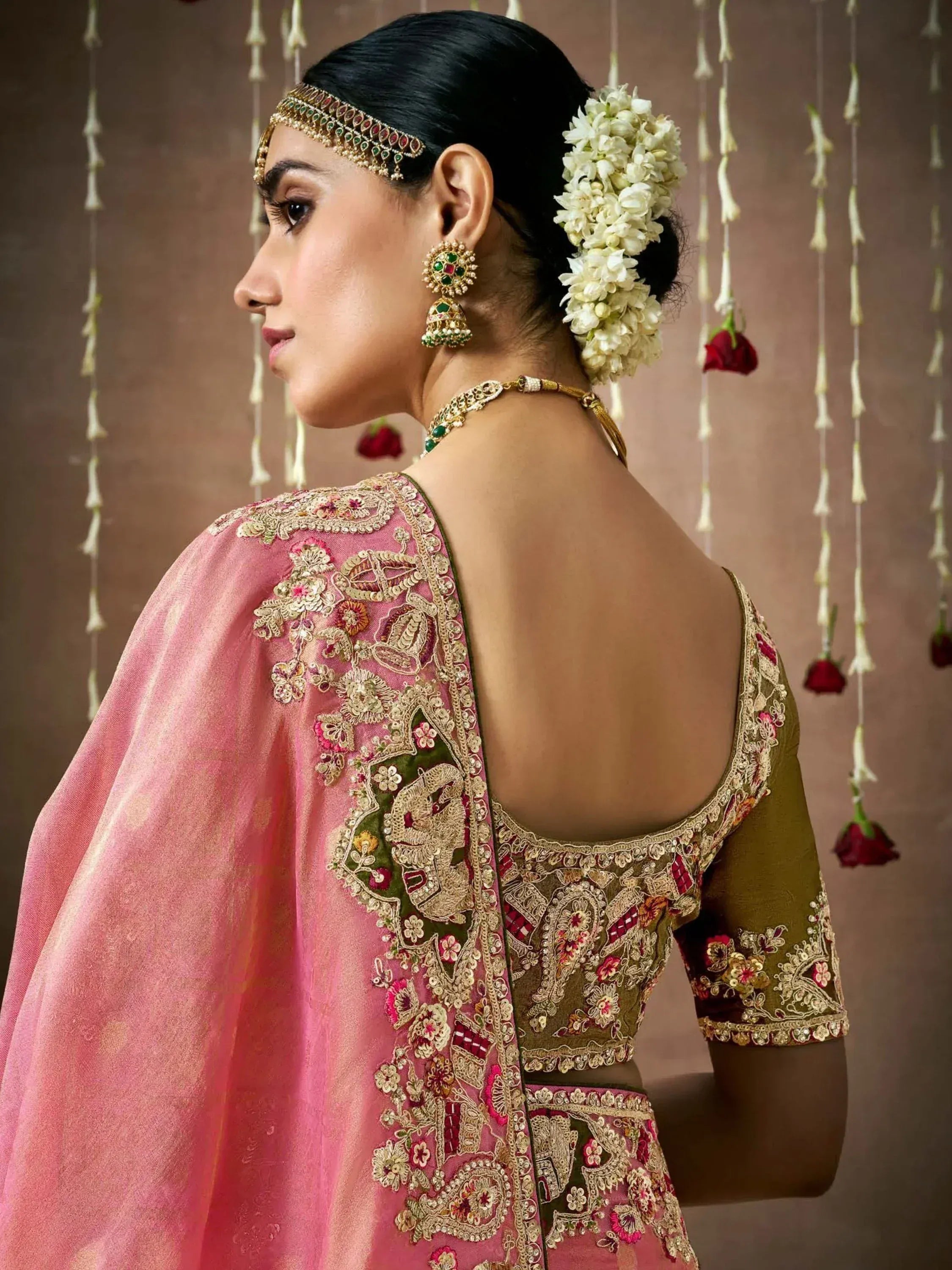 Woman in pink and olive green embroidered lehenga choli with floral jewelry and gajra, perfect for Indian weddings