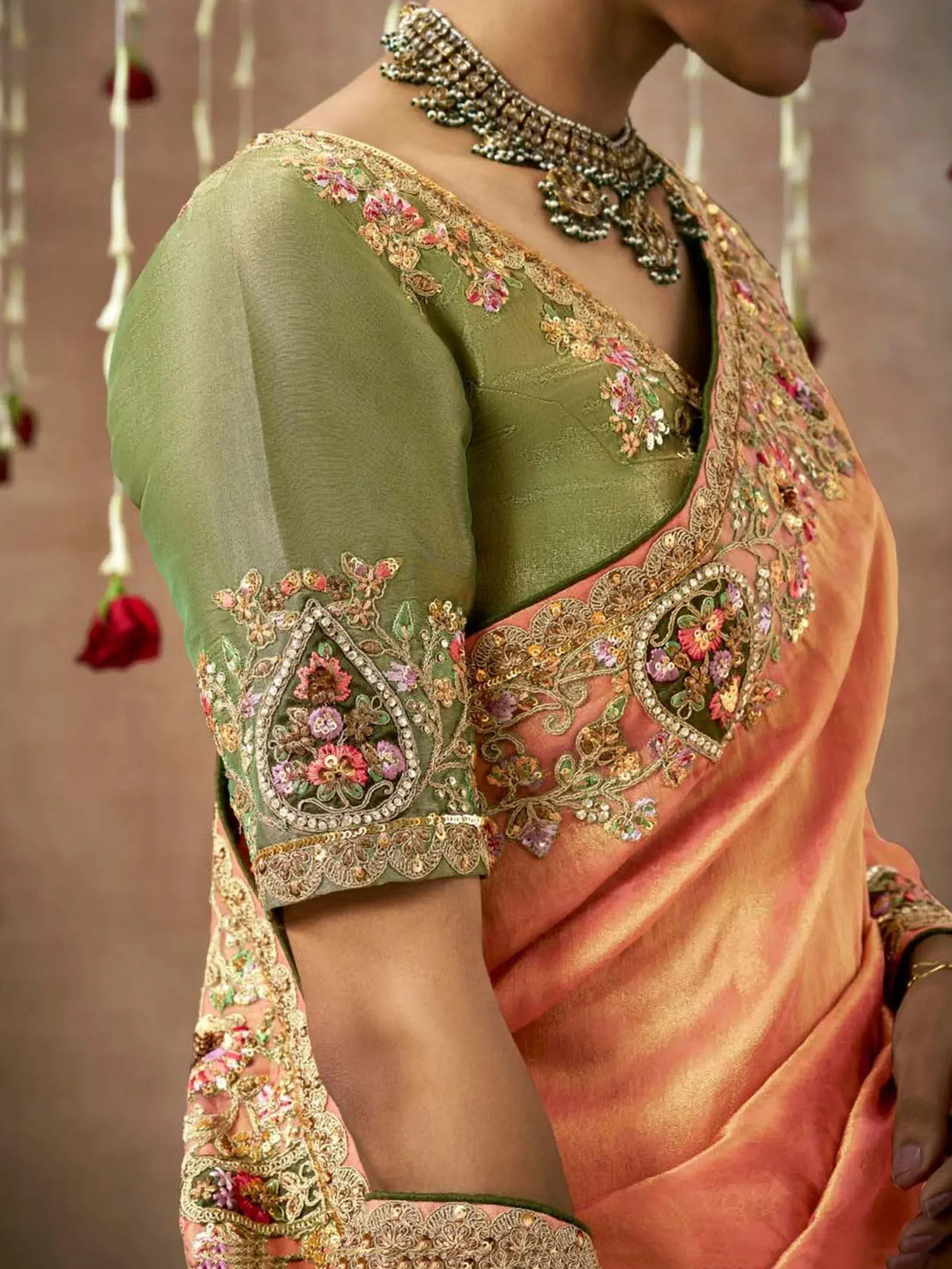 Olive green and peach designer saree with floral embroidery and gold detailing, paired with statement necklace.