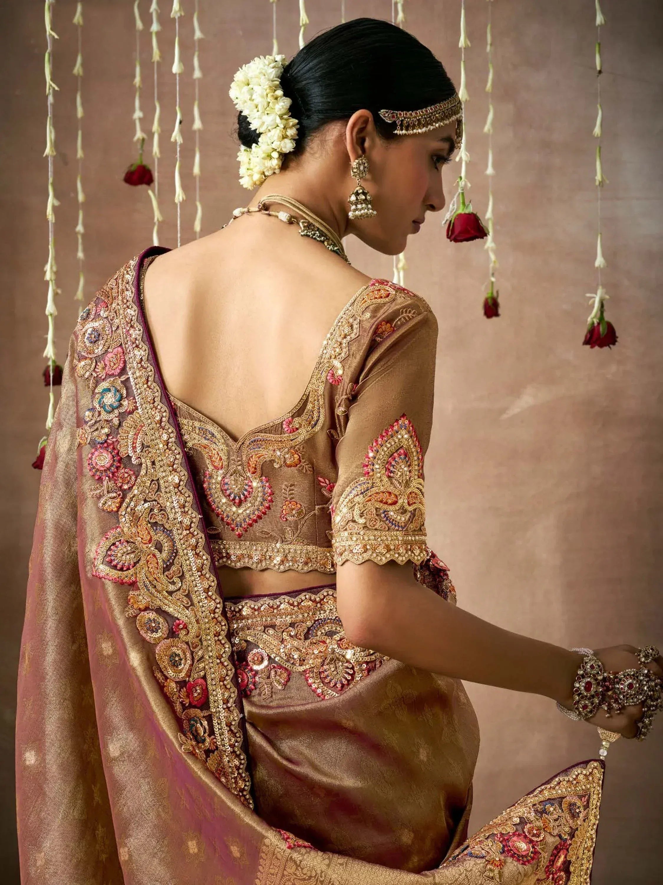 Elegant Indian bridal lehenga choli with intricate gold and pink embroidery, floral hair accessory, and traditional jewelry