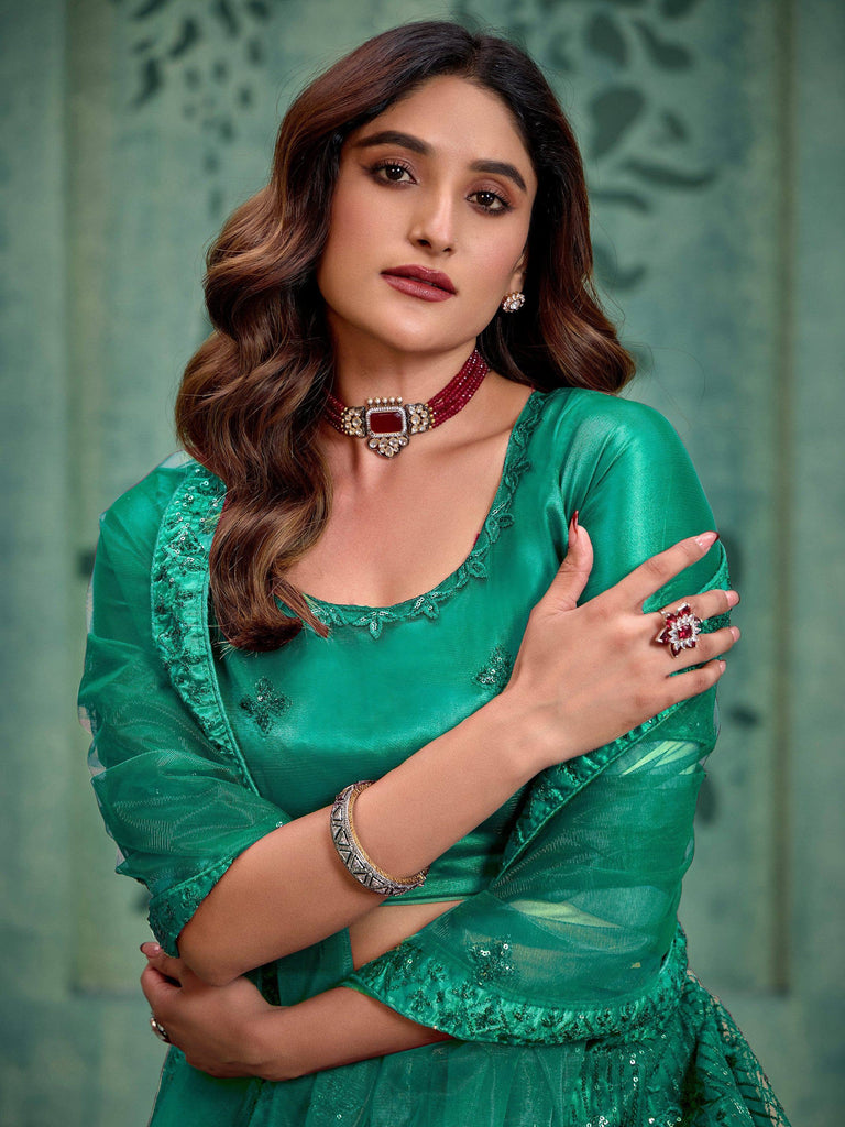 Emerald green ethnic gown with sequin detailing, paired with red gemstone jewelry for festive occasions.