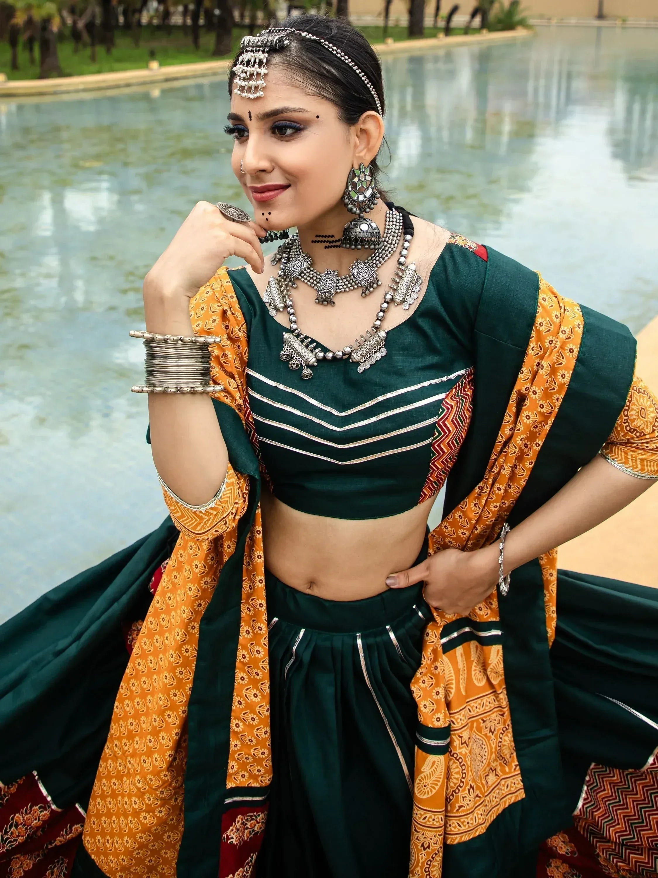 Woman in green and orange ethnic lehenga choli with silver jewelry by poolside