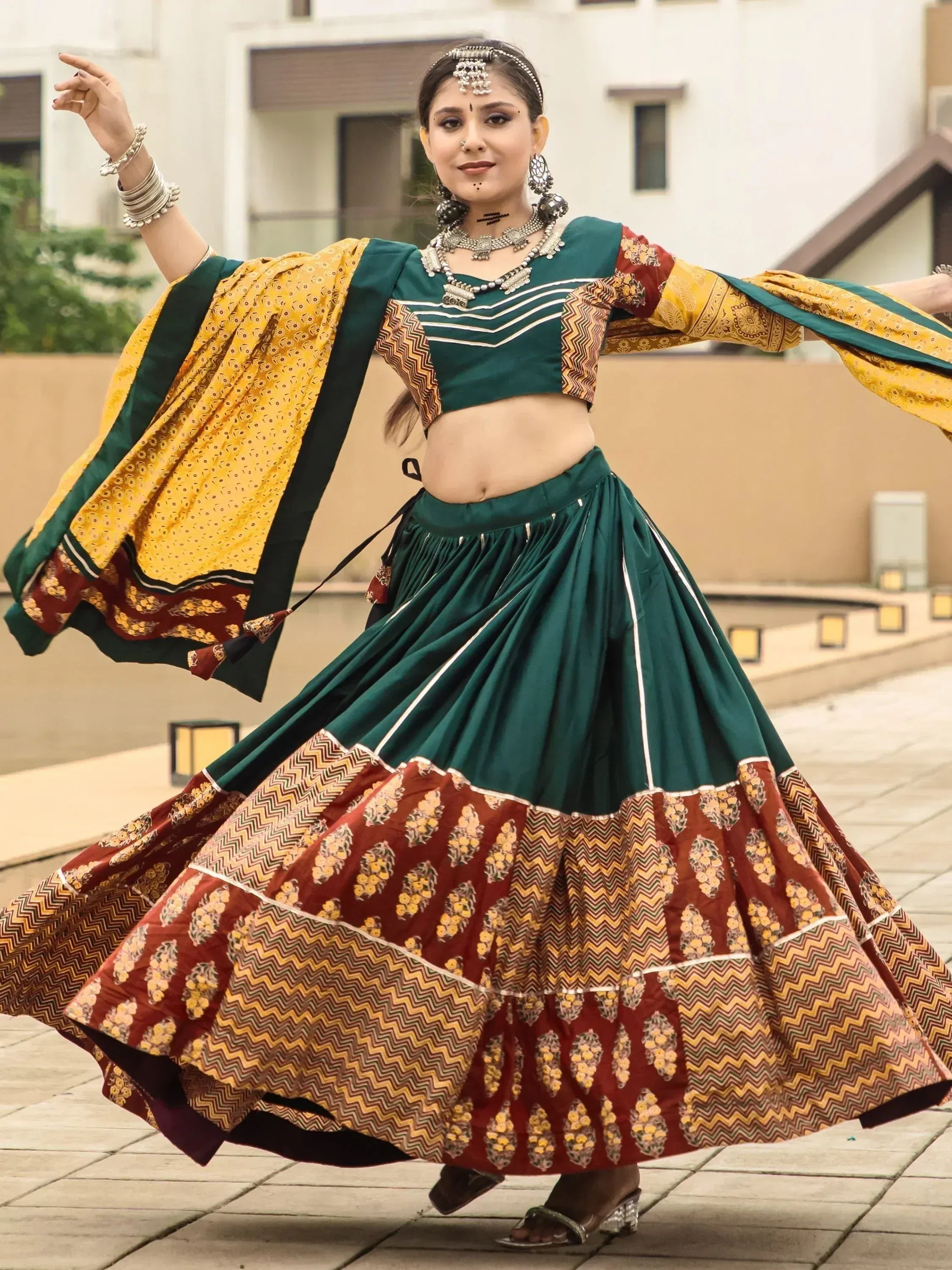 Woman in green and maroon Indian lehenga choli with yellow dupatta, dancing outdoors