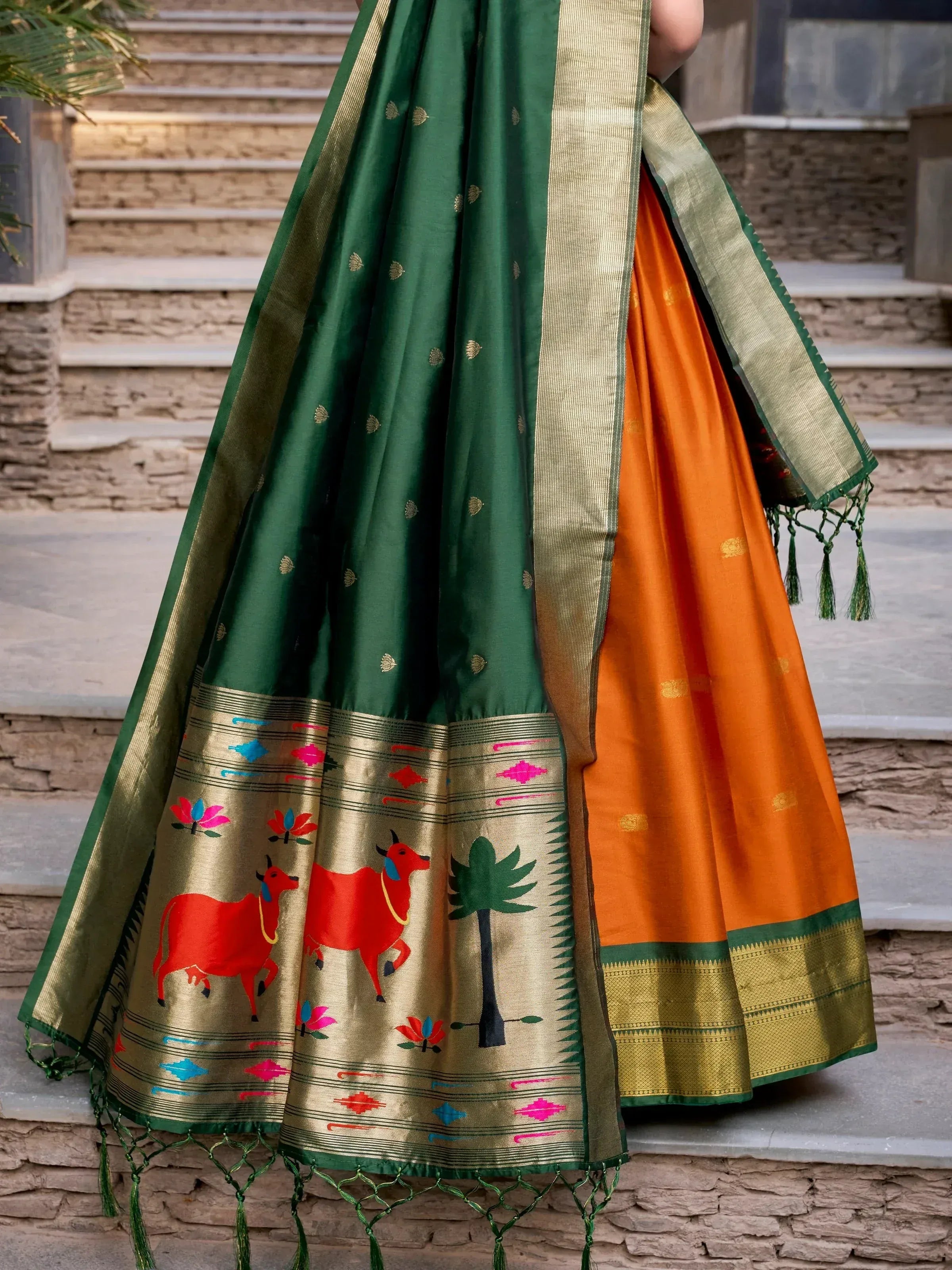Green and orange ethnic saree with cow and palm tree print, gold border, tassels, perfect for festive occasions.