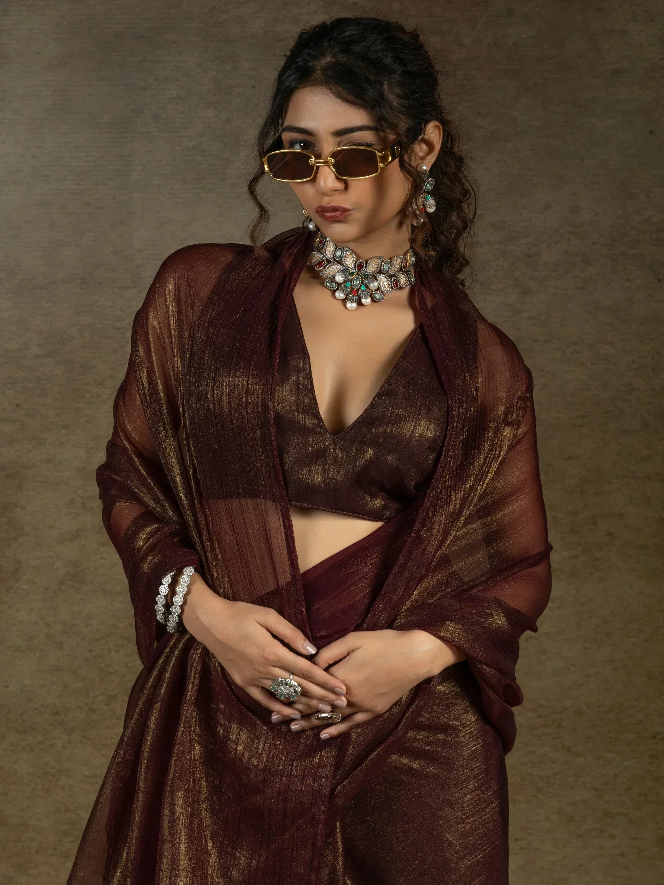 Woman in maroon ethnic saree with gold detailing, statement jewelry, and sunglasses