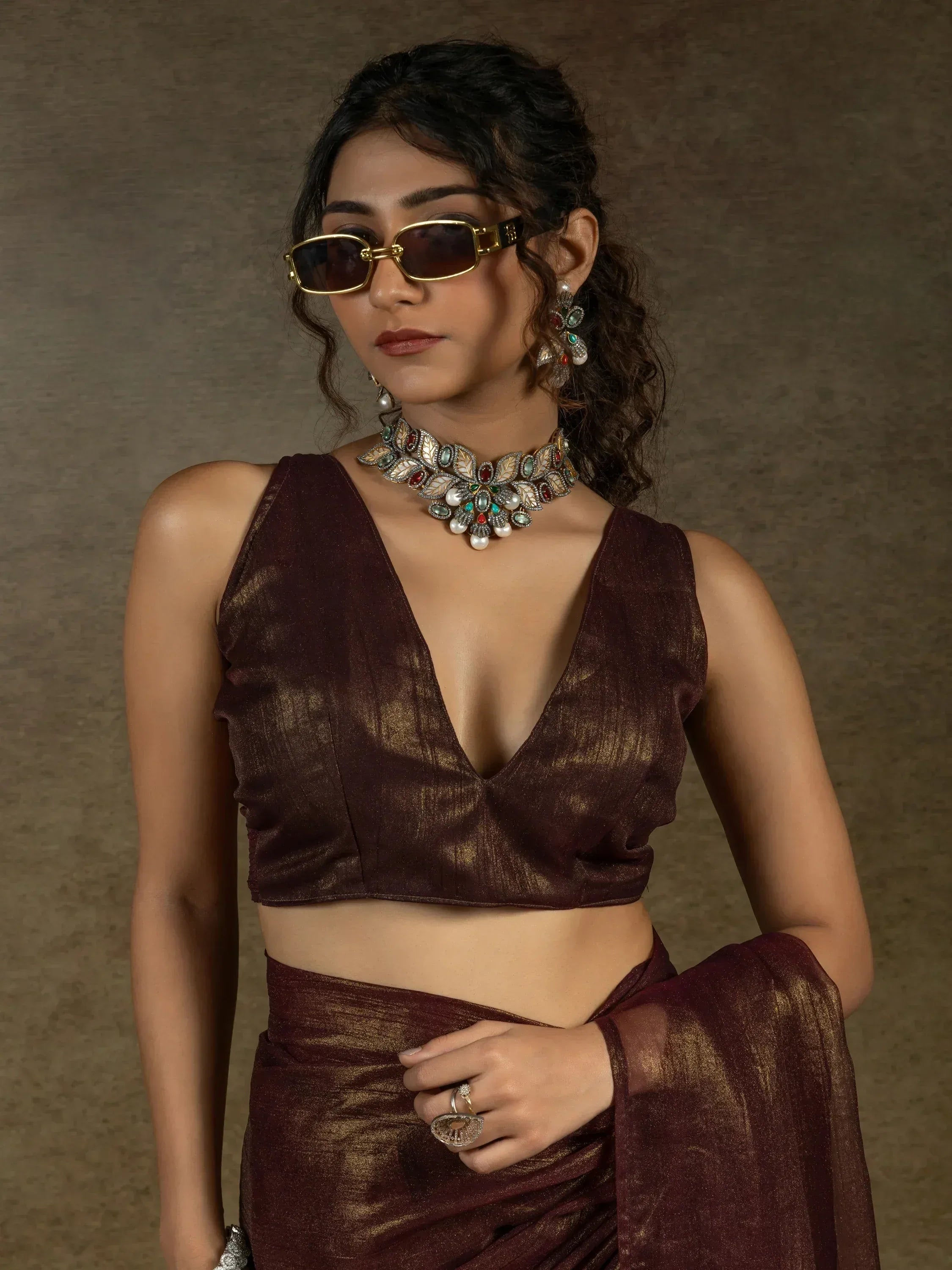 Woman in maroon saree with deep V blouse, statement jewelry, and sunglasses