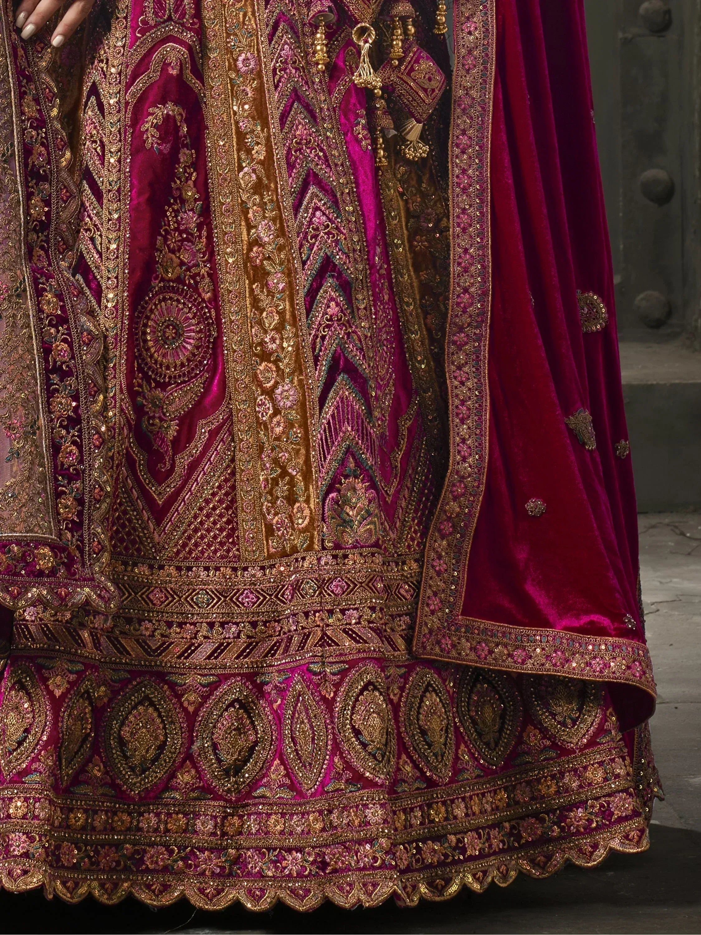 Luxury maroon velvet lehenga choli with heavy gold embroidery and sequins, perfect for Indian weddings.