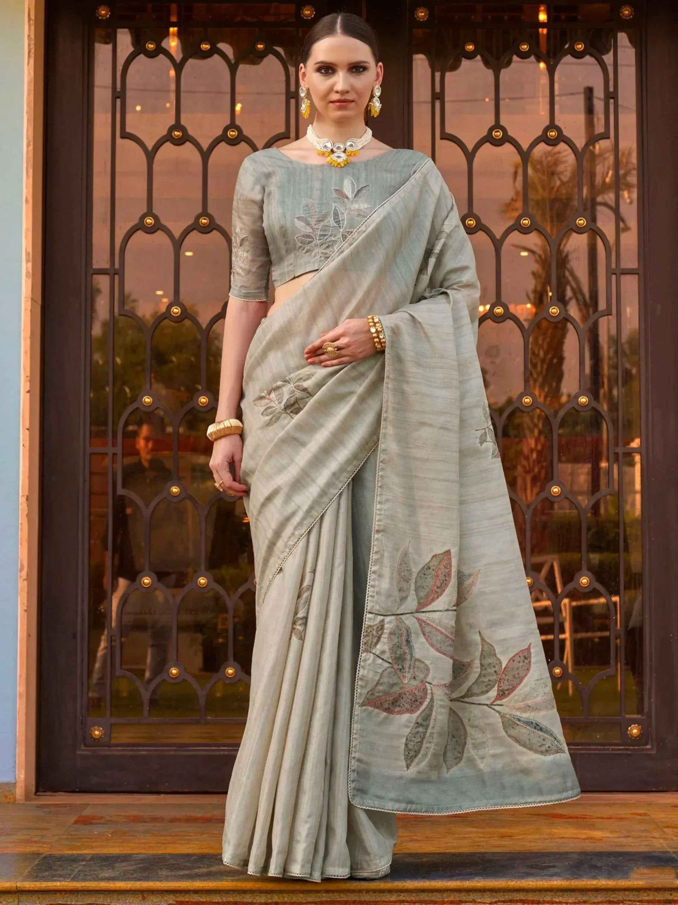 Elegant light grey saree with leaf embroidery, styled with gold jewelry for Indian ethnic wear